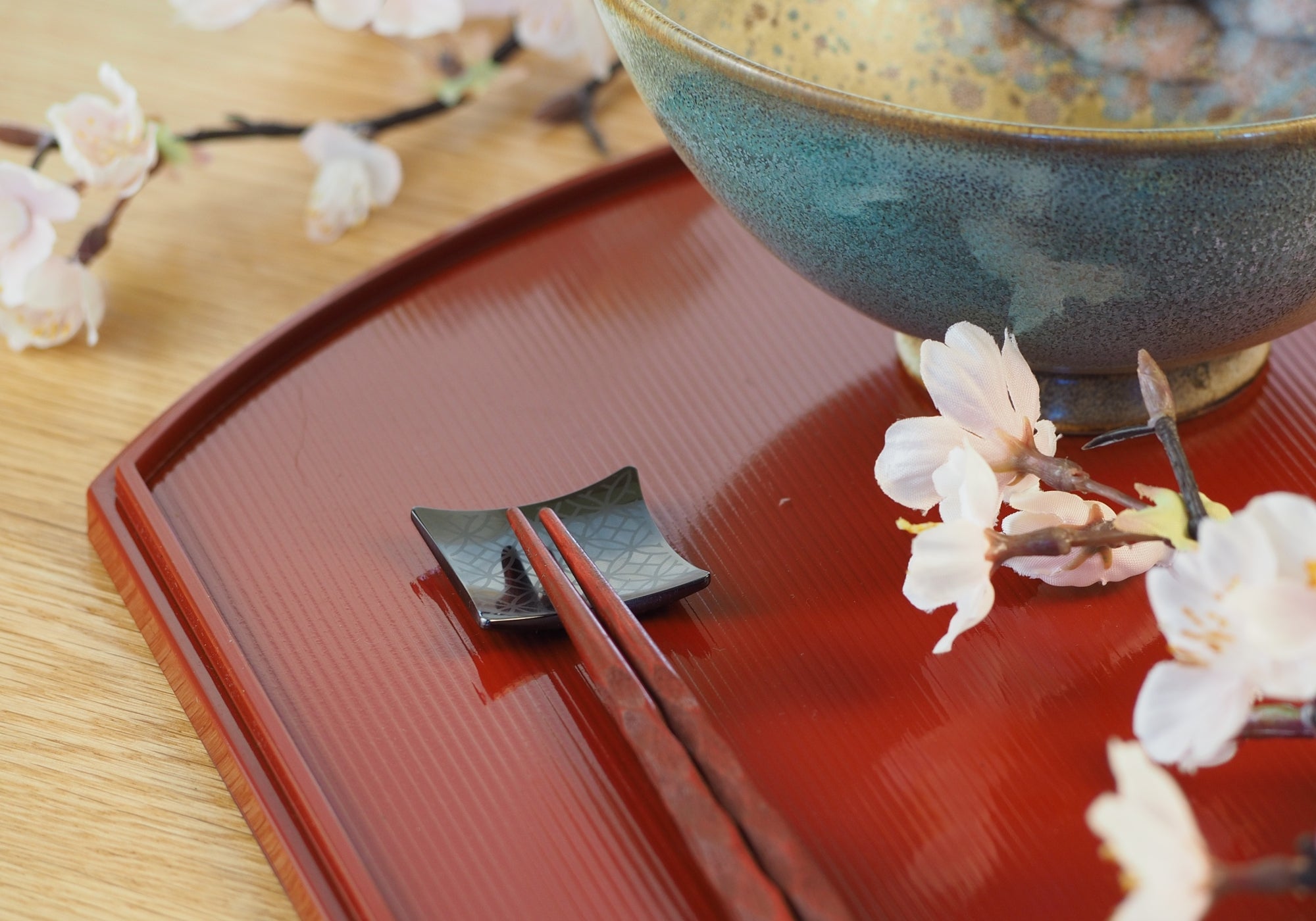 Close-up of a black Japanese chopstick rest with ceramic sakura bowl on a wooden surface. Tsukushi