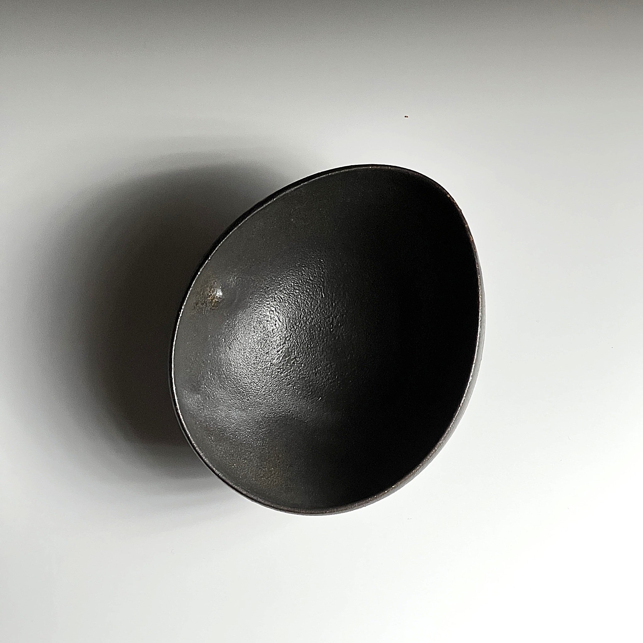 Top view of handcrafted black Japanese ceramic bowl on a white gradation background, Tsukushi