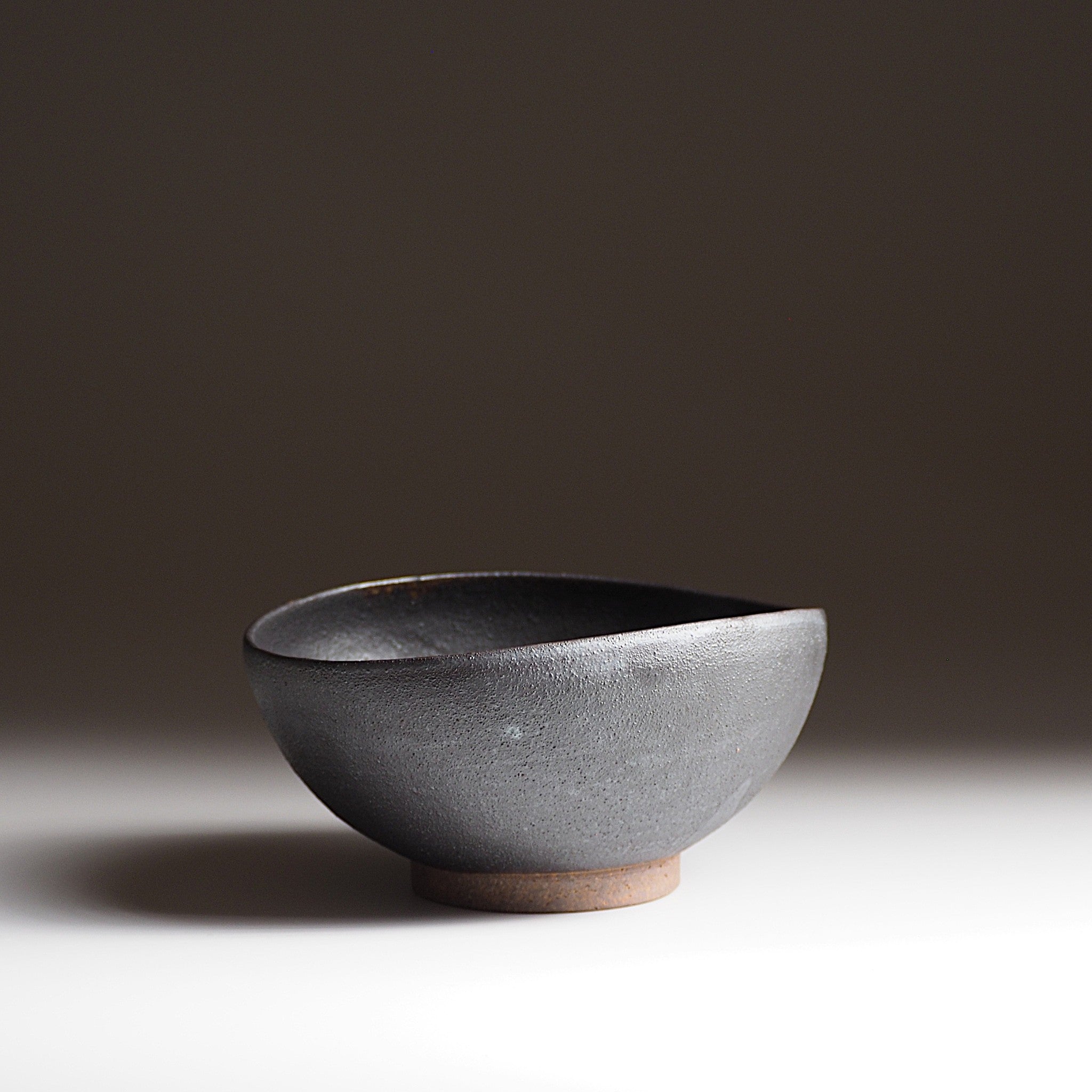 Side view of handcrafted black Japanese ceramic bowl on a dark gradation background, Tsukushi