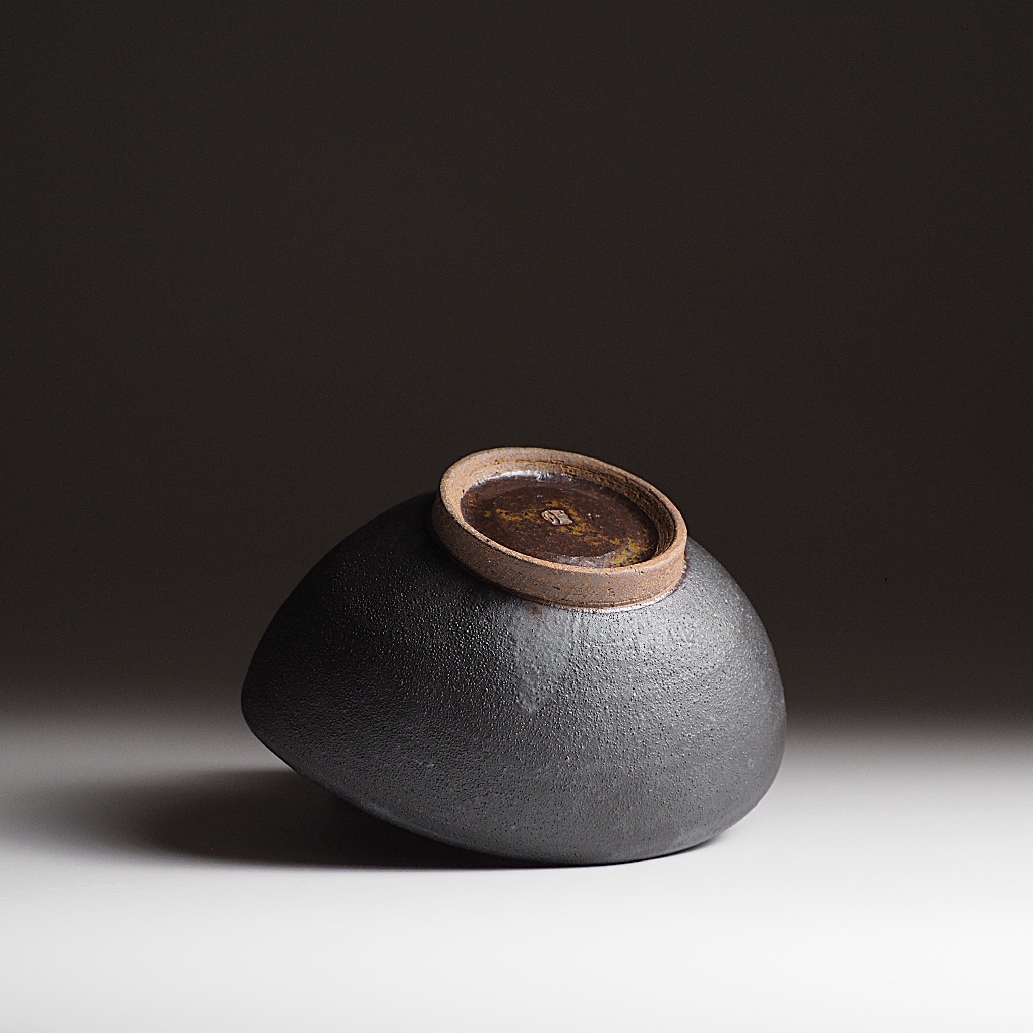 Handcrafted black Japanese ceramic bowl with a brown bottom on a dark gradation background, Tsukushi