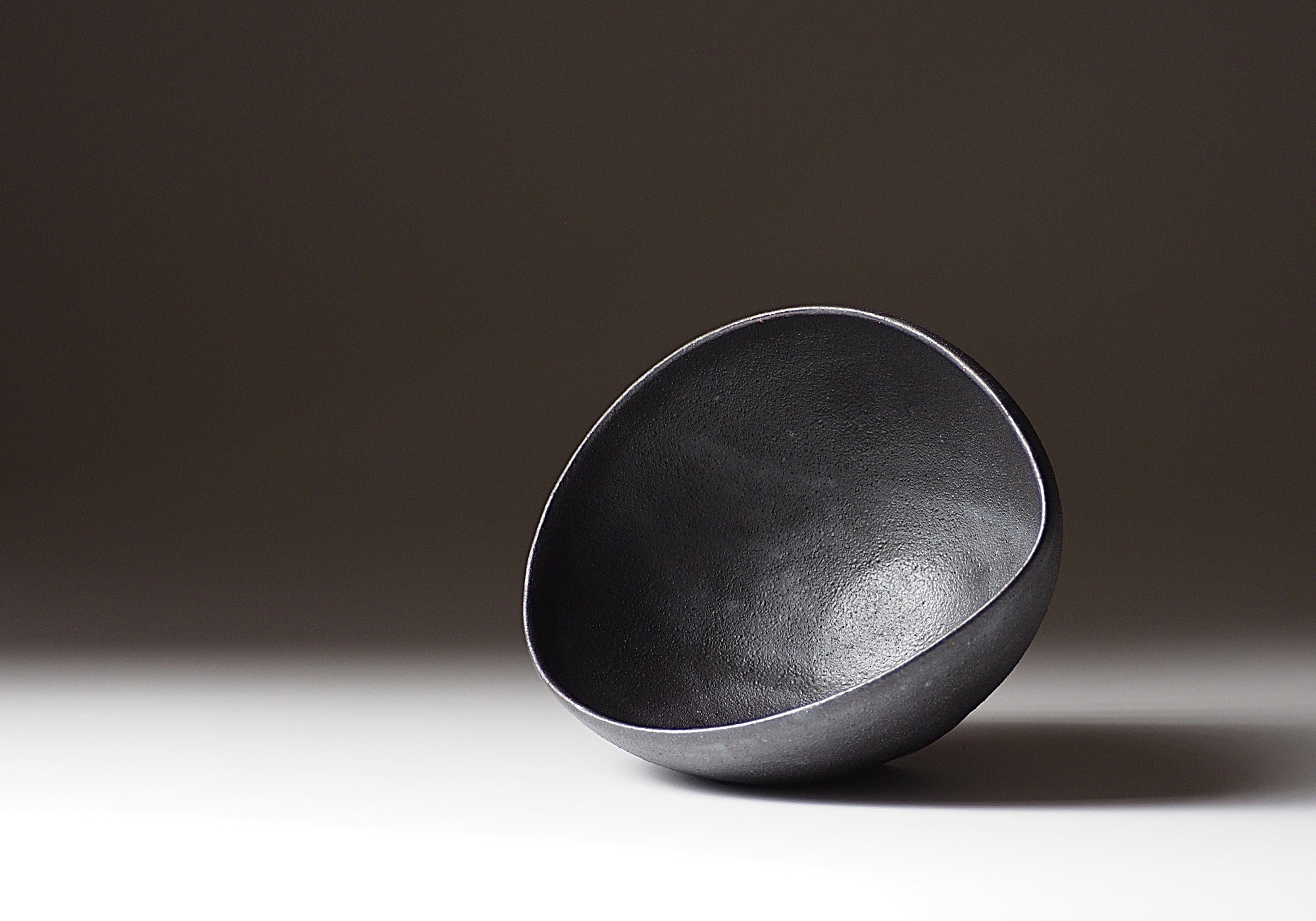 Handcrafted Japanese black ceramic bowl on a gradient background, Tsukushi