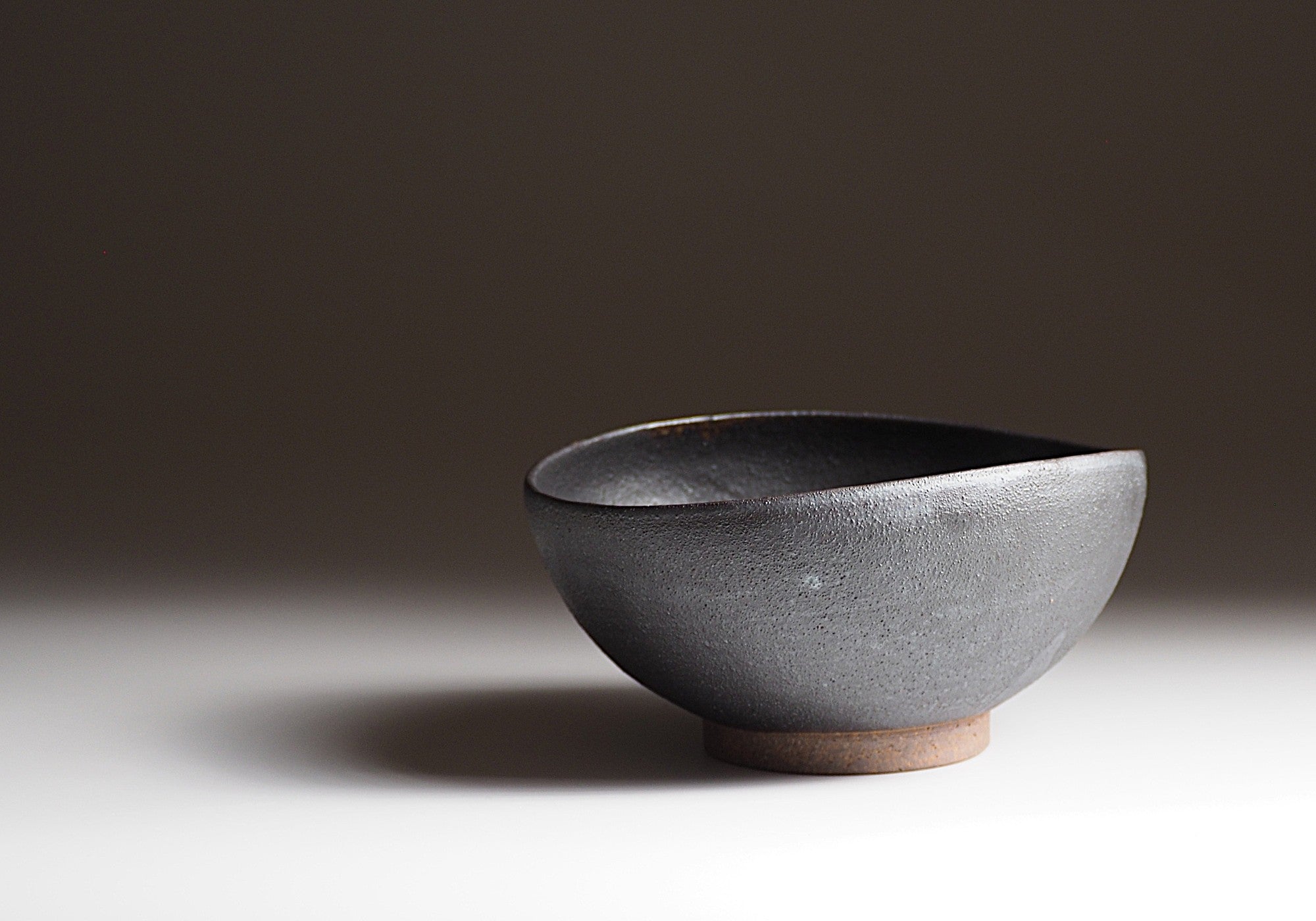 Handcrafted Japanese black ceramic bowl on a neutral background with shadow, Tsukushi