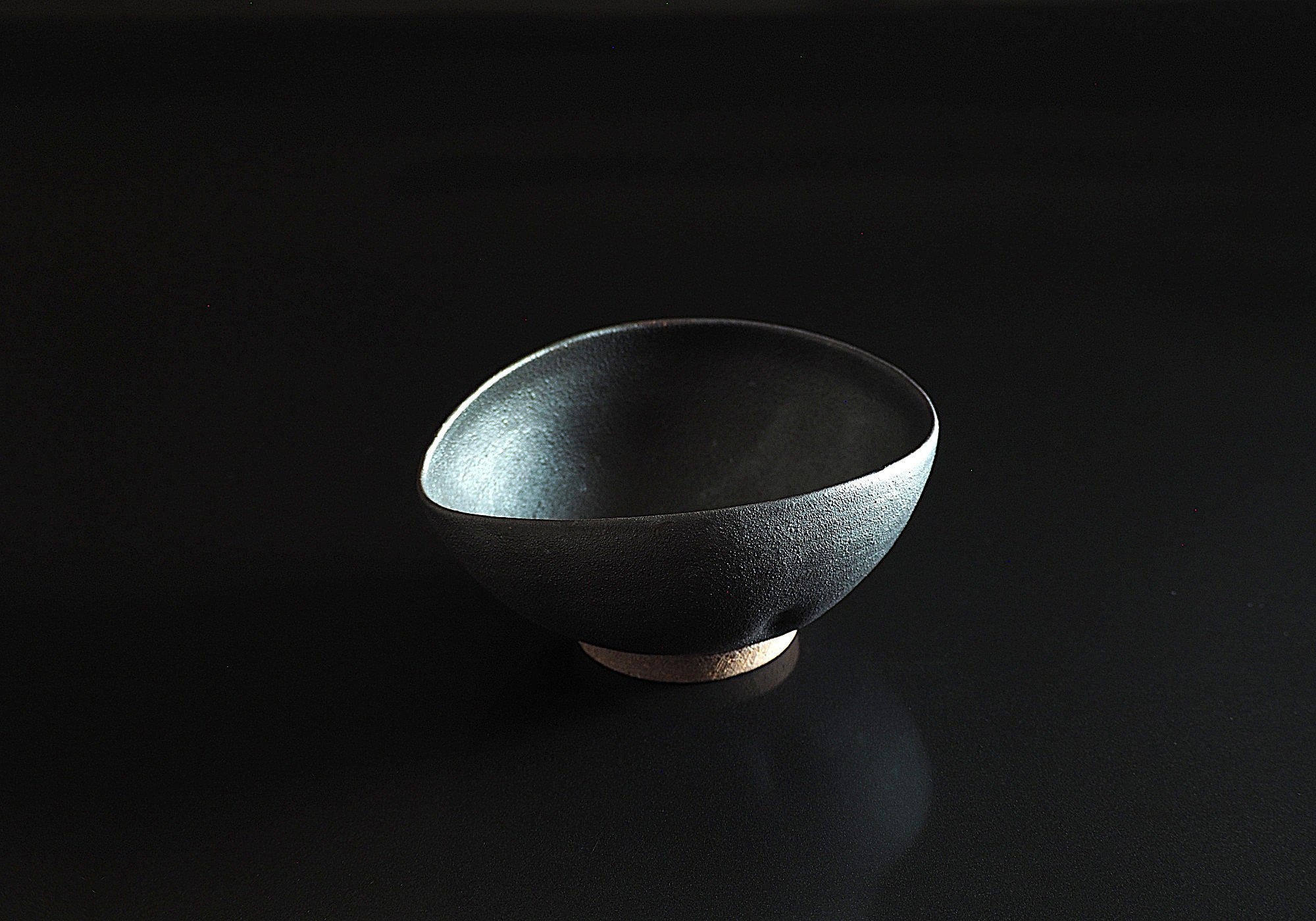 Black ceramic cereal bowl on a dark background. Tsukushi
