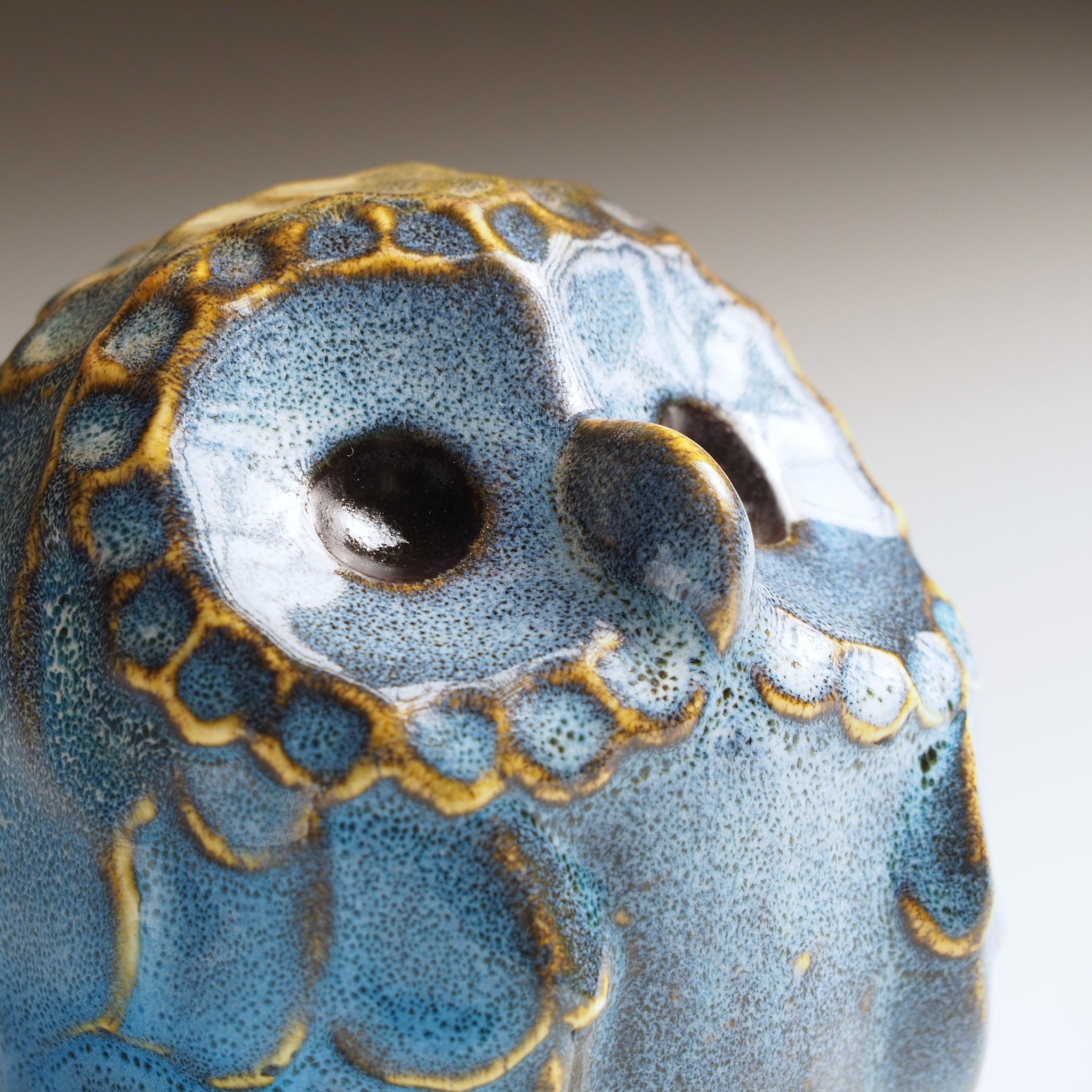 Side detail of the small Fukumori ceramic owl figurine with blue and gold patterns on a neutral background