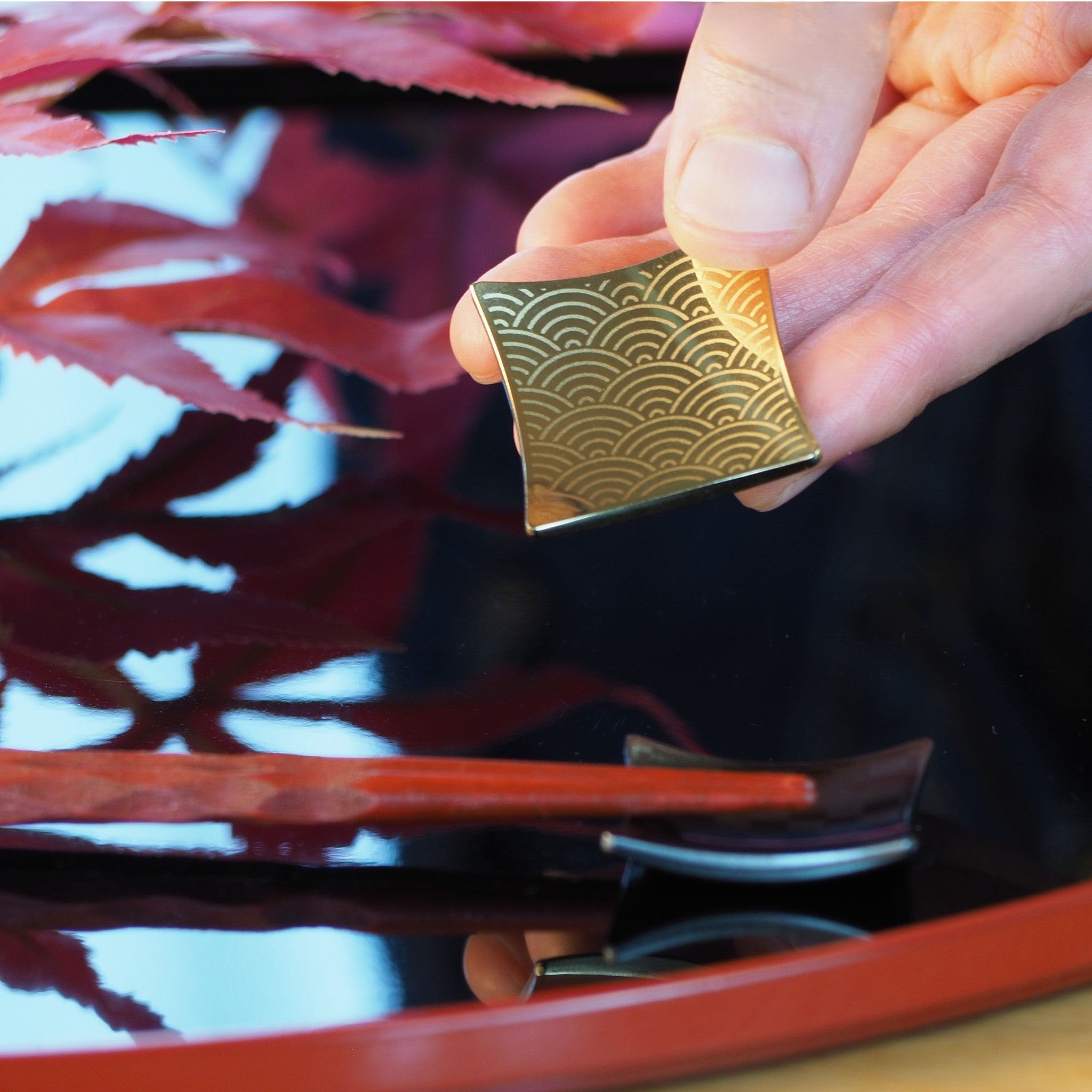 A gold Japanese chopstick rest held by a hand with a blurred background. Tsukushi
