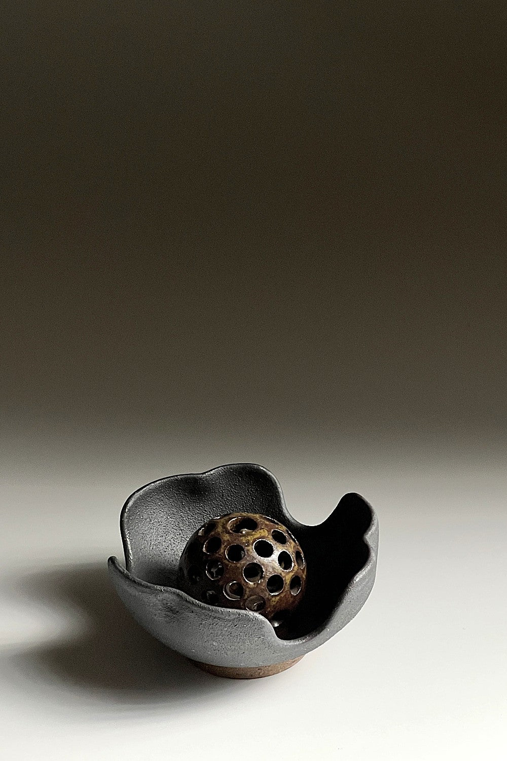 Bird’s-eye view of a black ikebana vase made of unglazed pottery on a faded background. Tsukushi.
