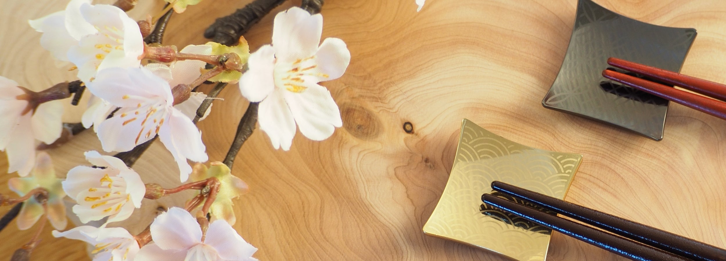 Cherry blossom branch with Japanese chopsticks and two chopstick rests on a wooden surface. Tsukushi