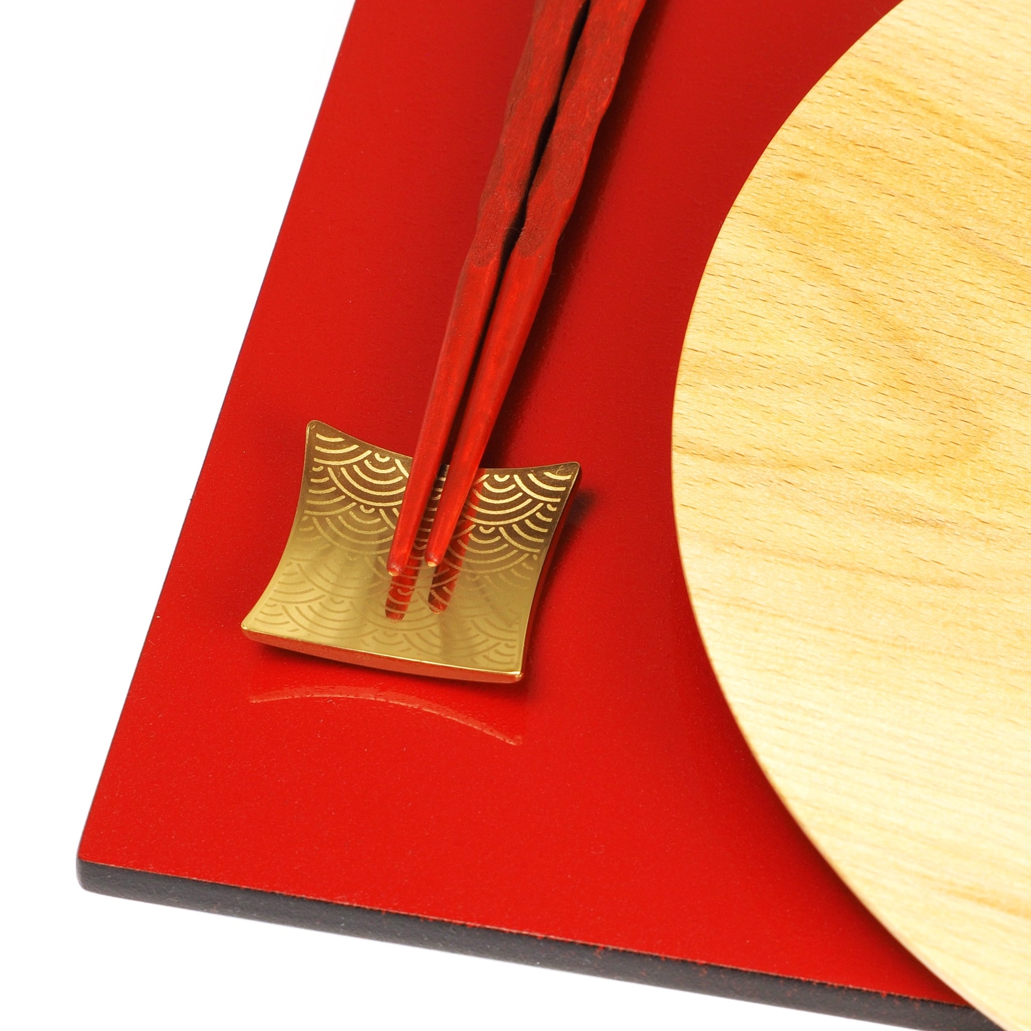 Close-up of a wooden plate with a red tray and gold Japanese chopstick rest. Tsukushi