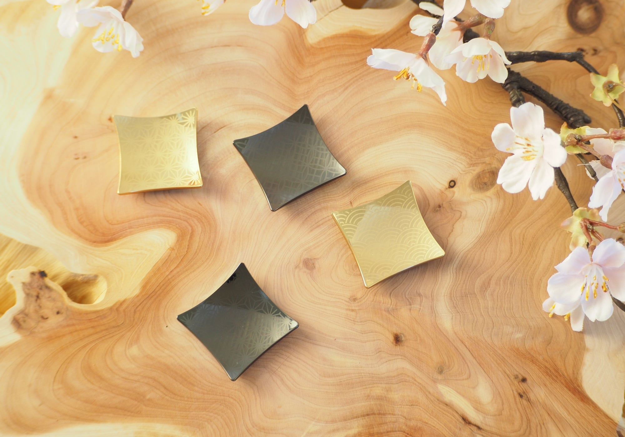Four black and gold Japanese chopstick rests placed on a wooden surface with sakura. Tsukushi