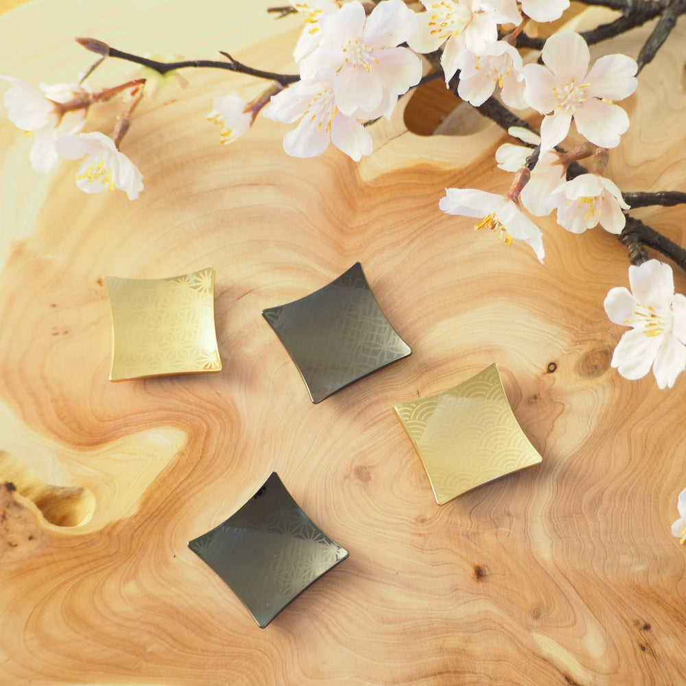 Four black and gold Japanese chopstick rests on a wooden surface with cherry blossoms. Tsukushi