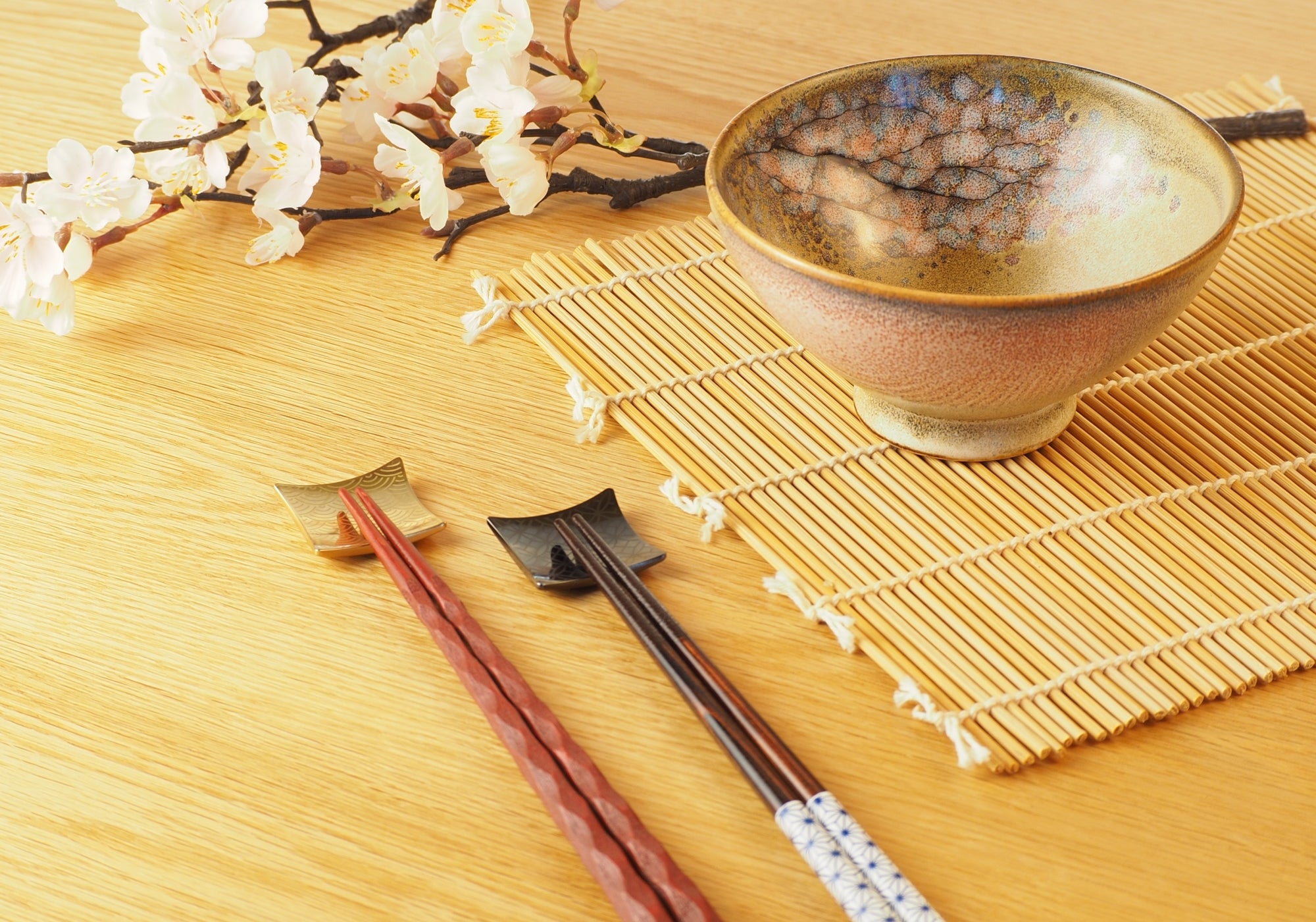 A Japanese ceramic bowl and chopsticks on a bamboo mat with decorative flowers. Tsukushi