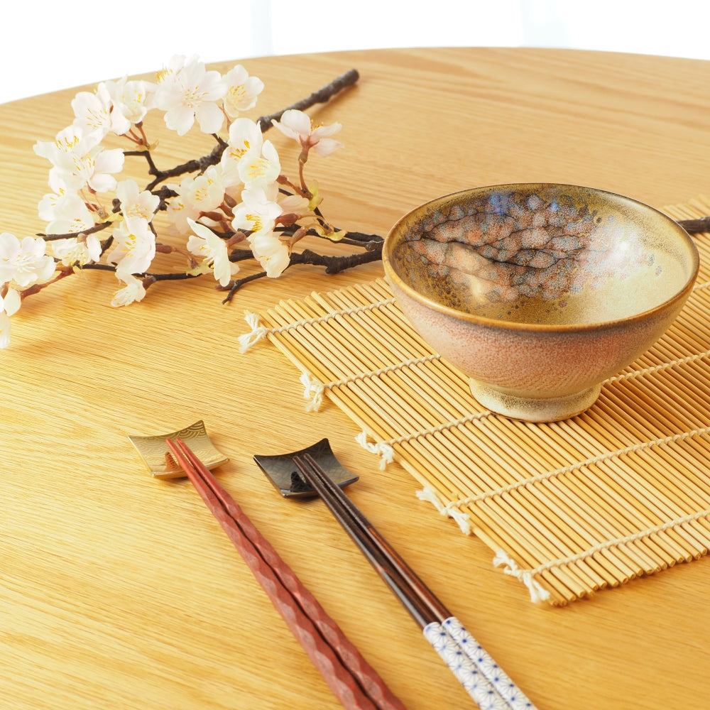 A Japanese ceramic bowl and chopsticks on a wooden table with decorative flowers. Tsukushi