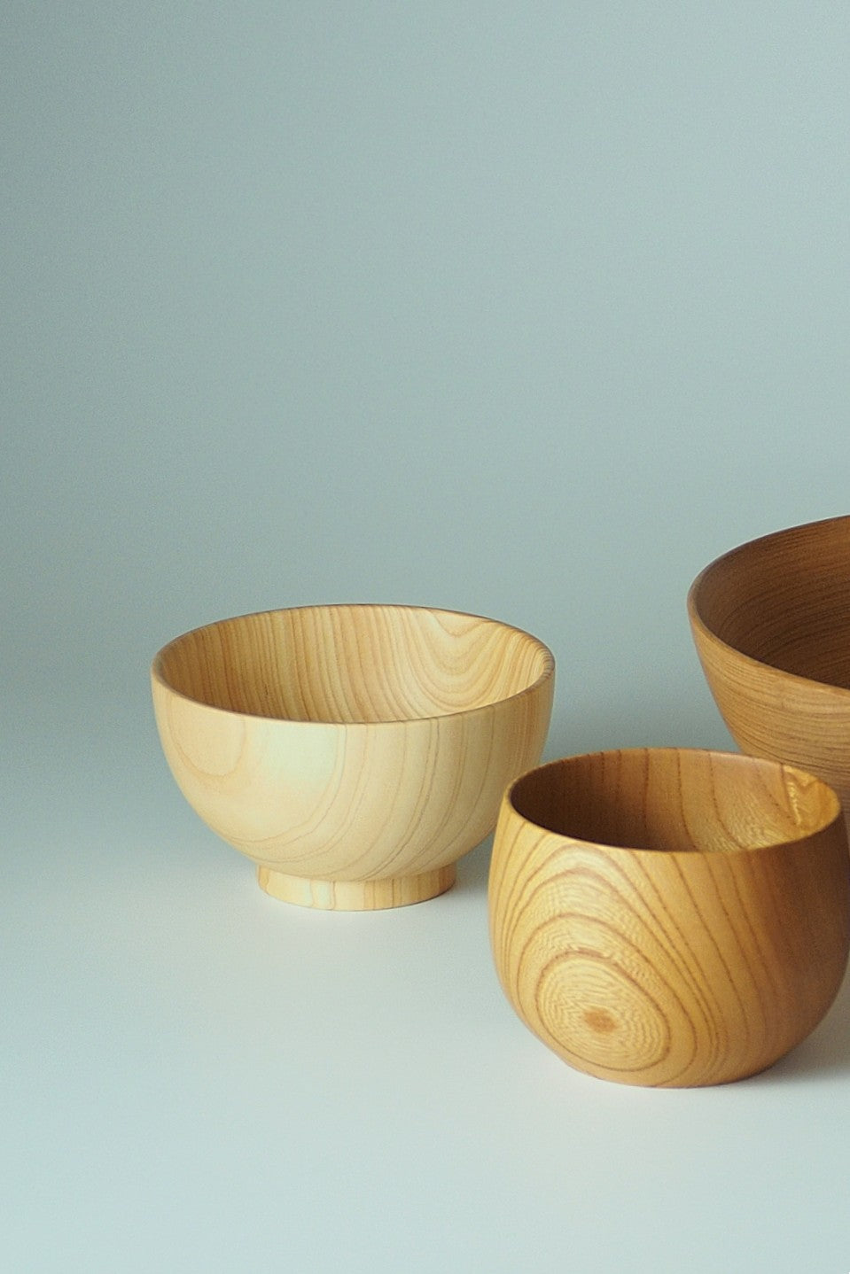 Three Japanese wooden bowls of different sizes on a light gray background. Tsukushi