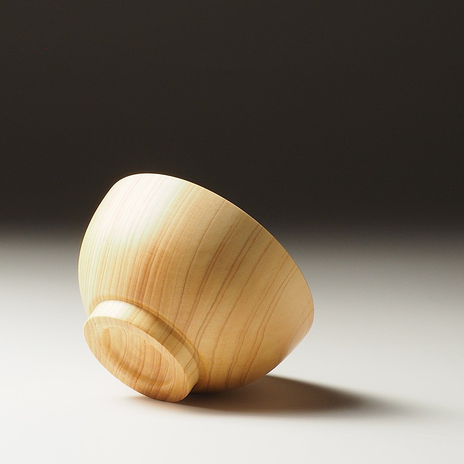 A bottom view of a Japanese wooden macha tea bowl on a beige background. Tsukushi