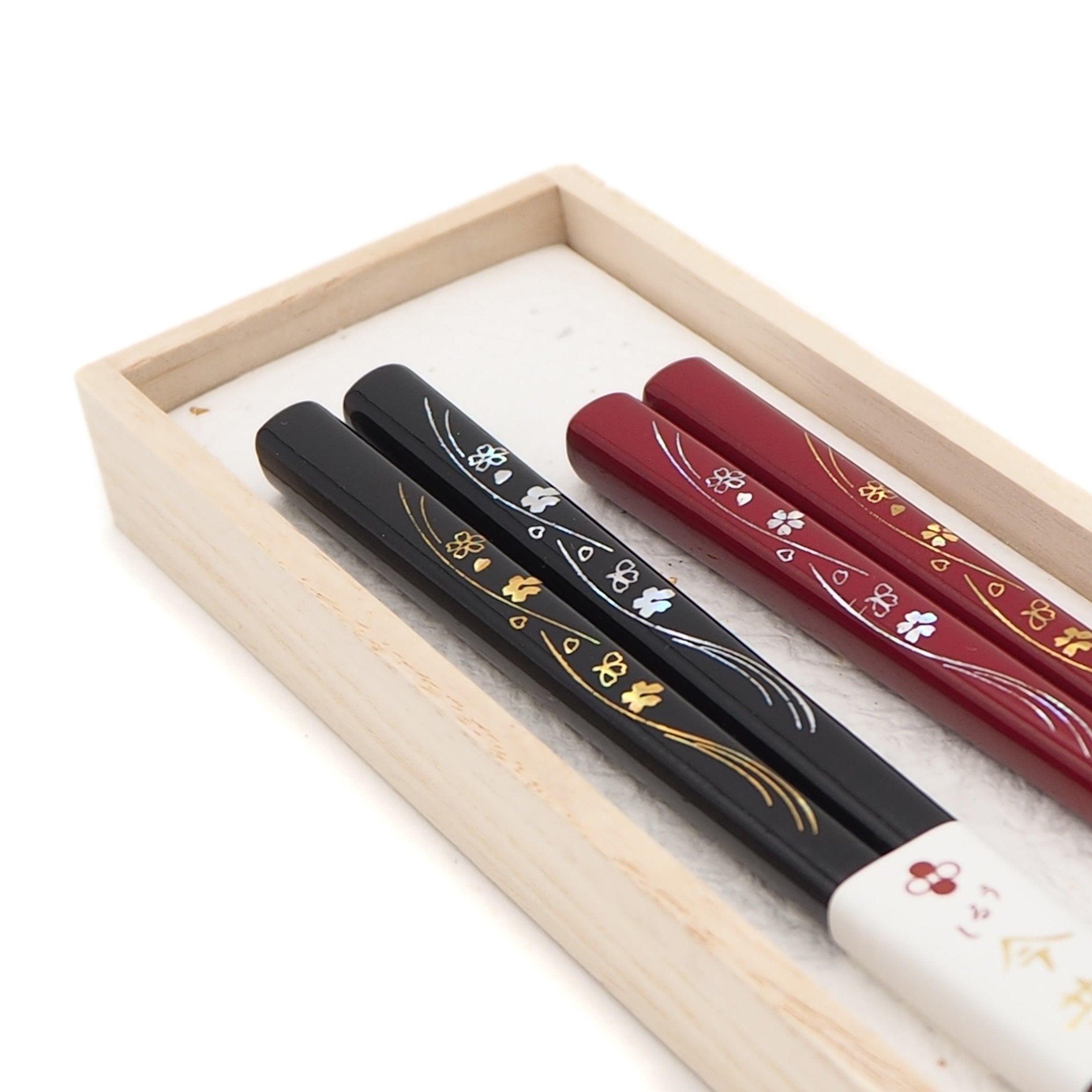 Detail of red and black Japanese chopsticks with cherry blossom motifs in box.