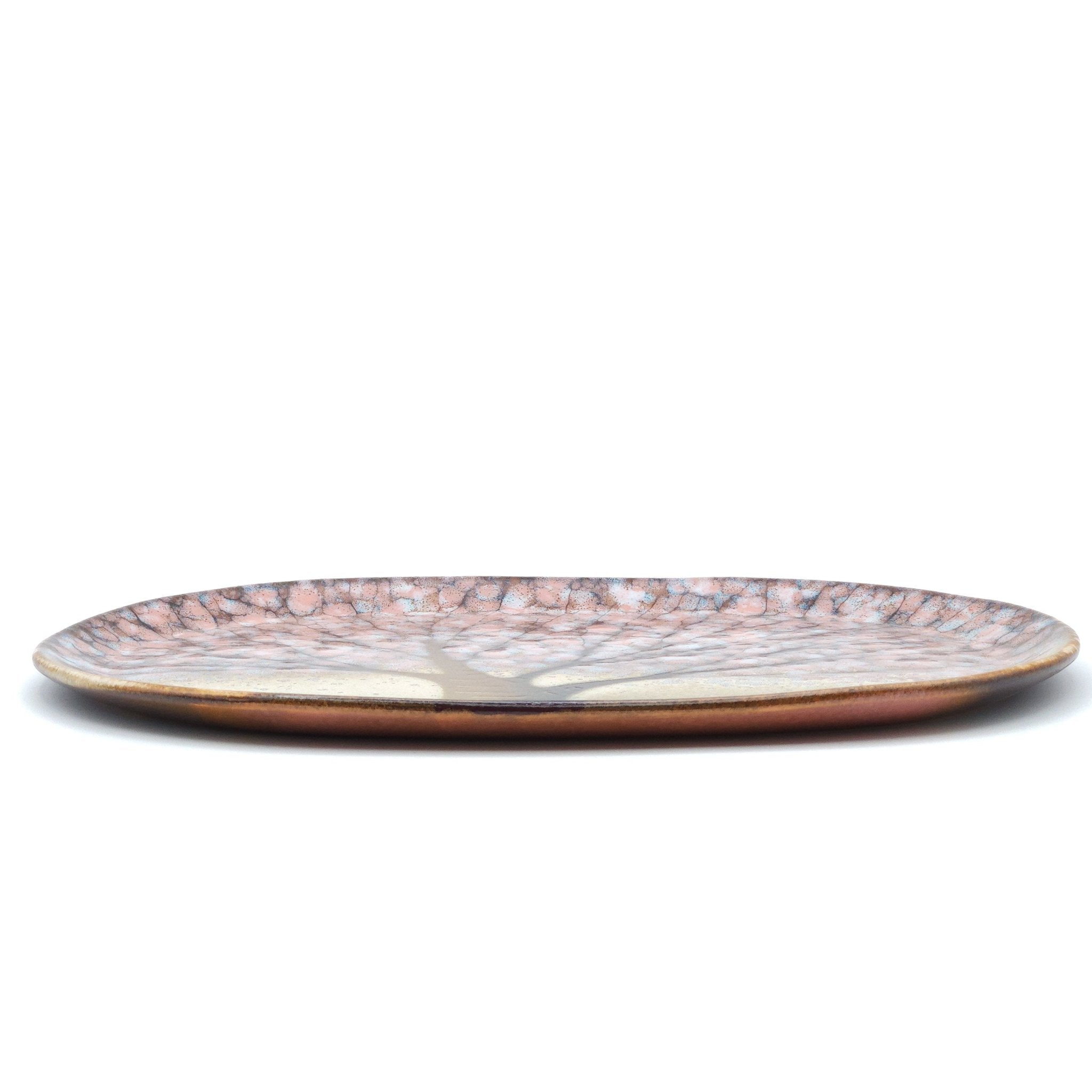 A Japanese plate made of pottery with cherry blossoms motif in  pink background. Long side view
