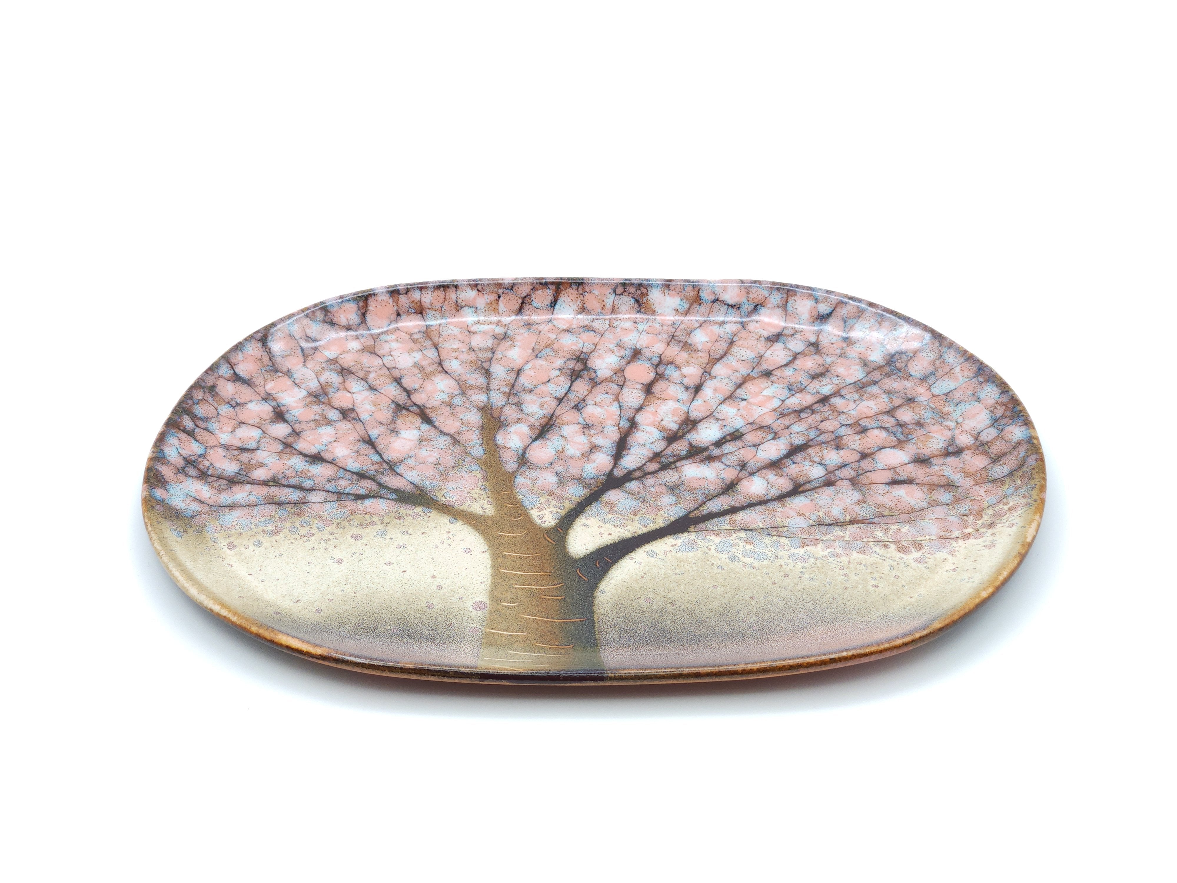 A Japanese plate made of pottery with cherry blossoms motif in pink background. Top long side view