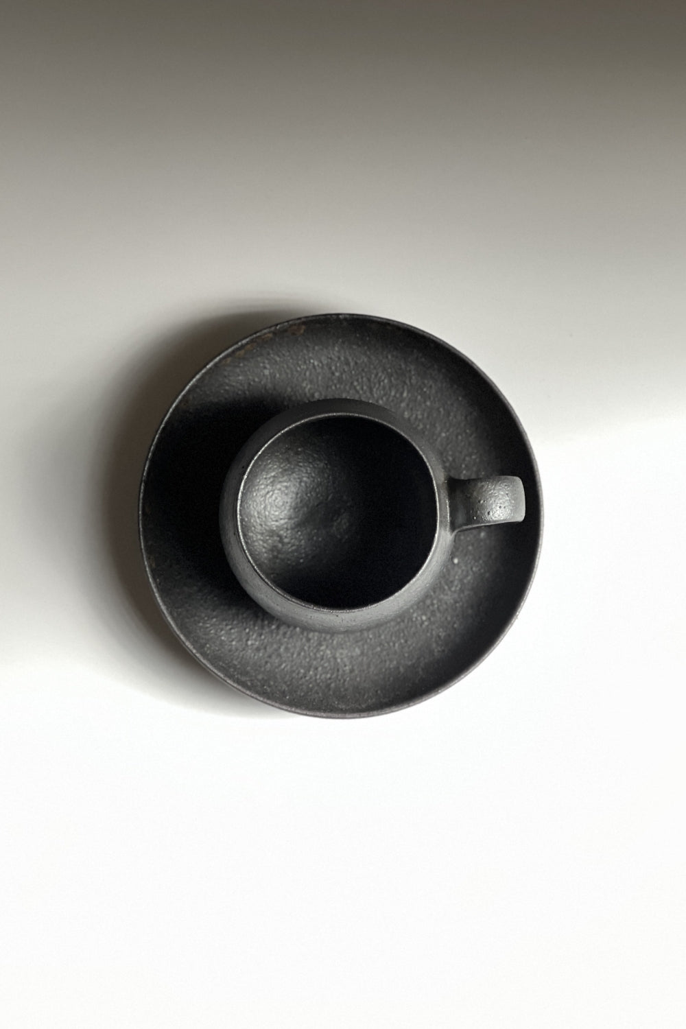 Top view of handcrafted black Japanese ceramic espresso cup and saucer on a light gray background, Tsukushi