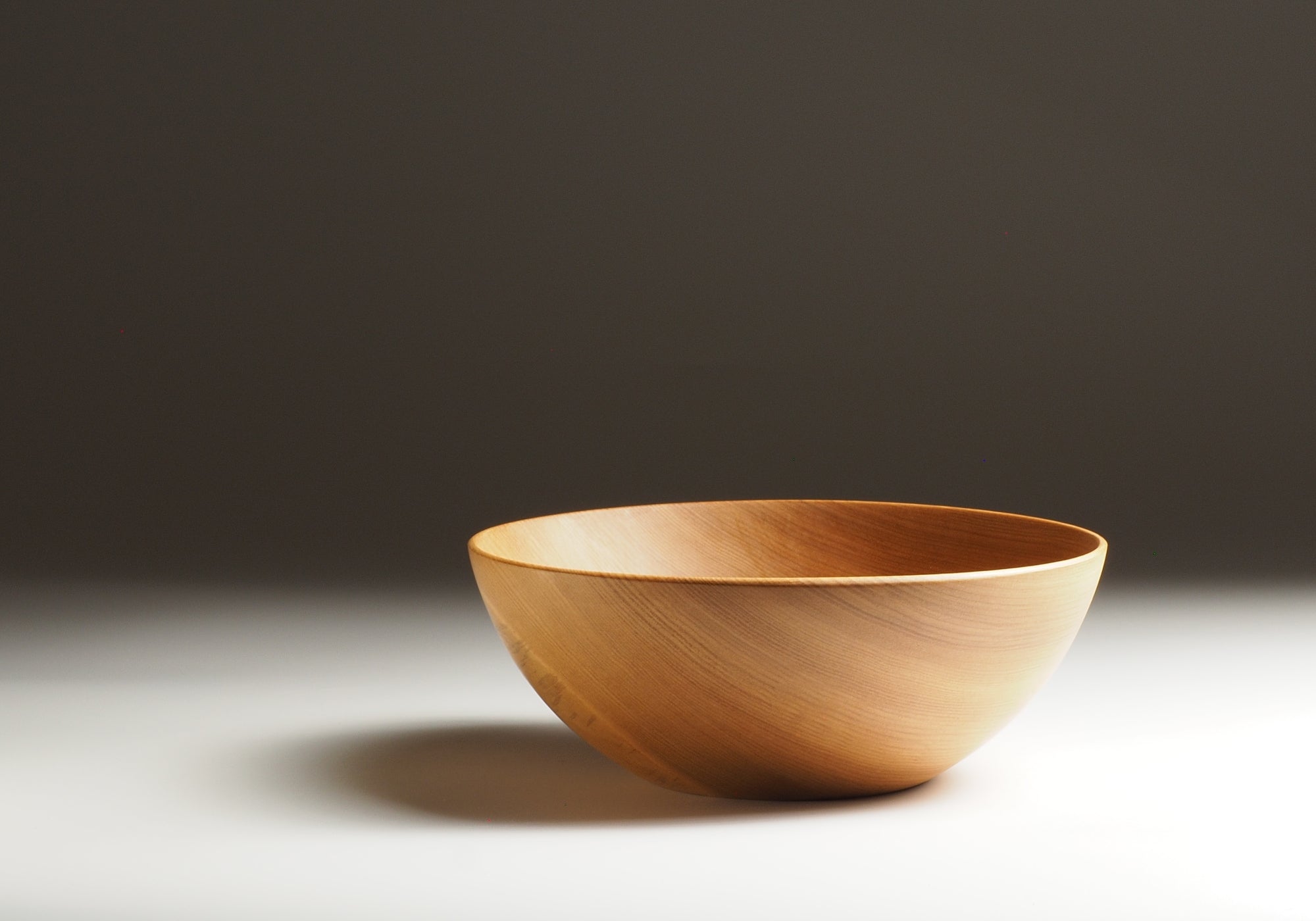 Side view of a Japanese wooden bowl against a beige gradation background. Tsukushi