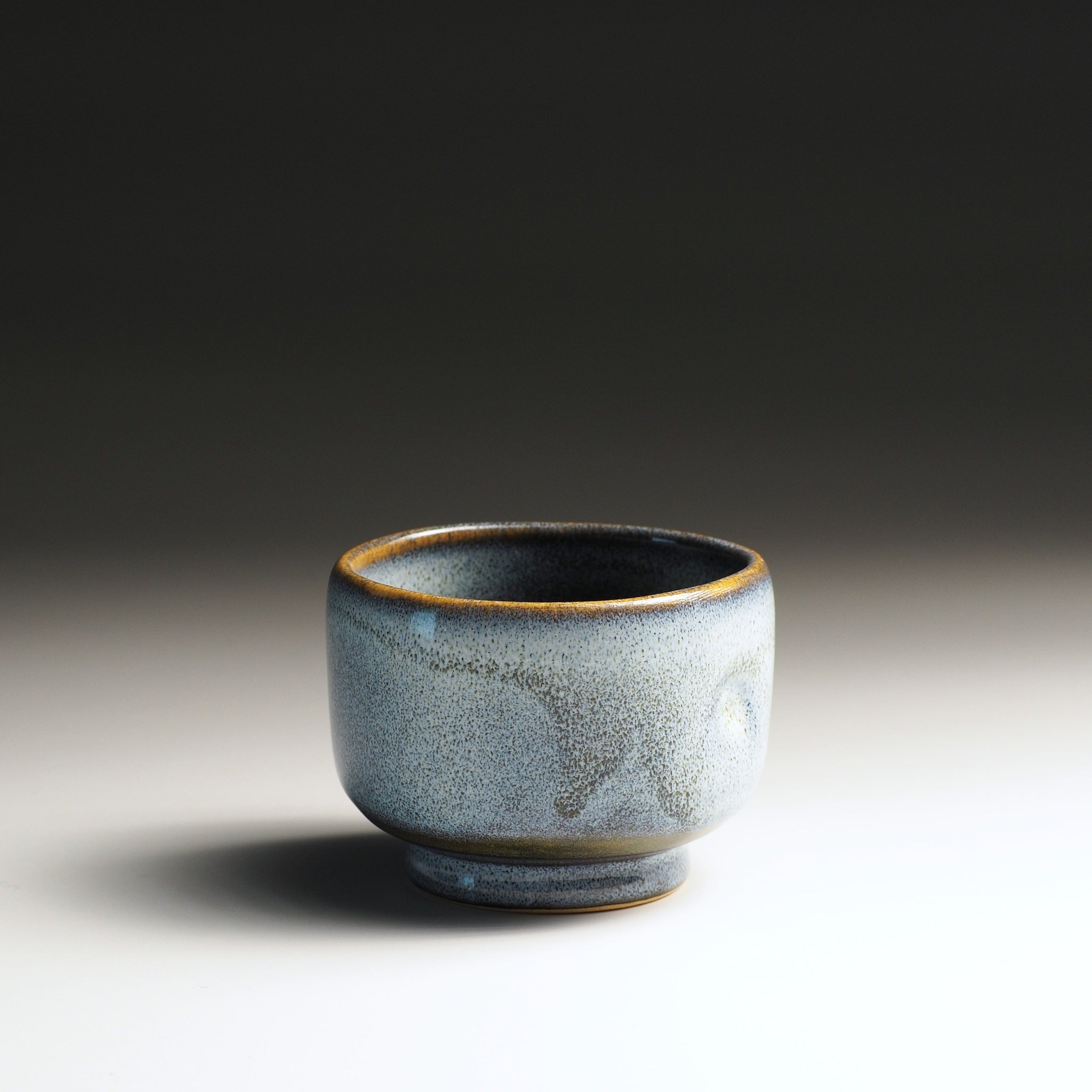 Front view of a Japanese ceramic teacup with wabi sabi glaze on a gradient background