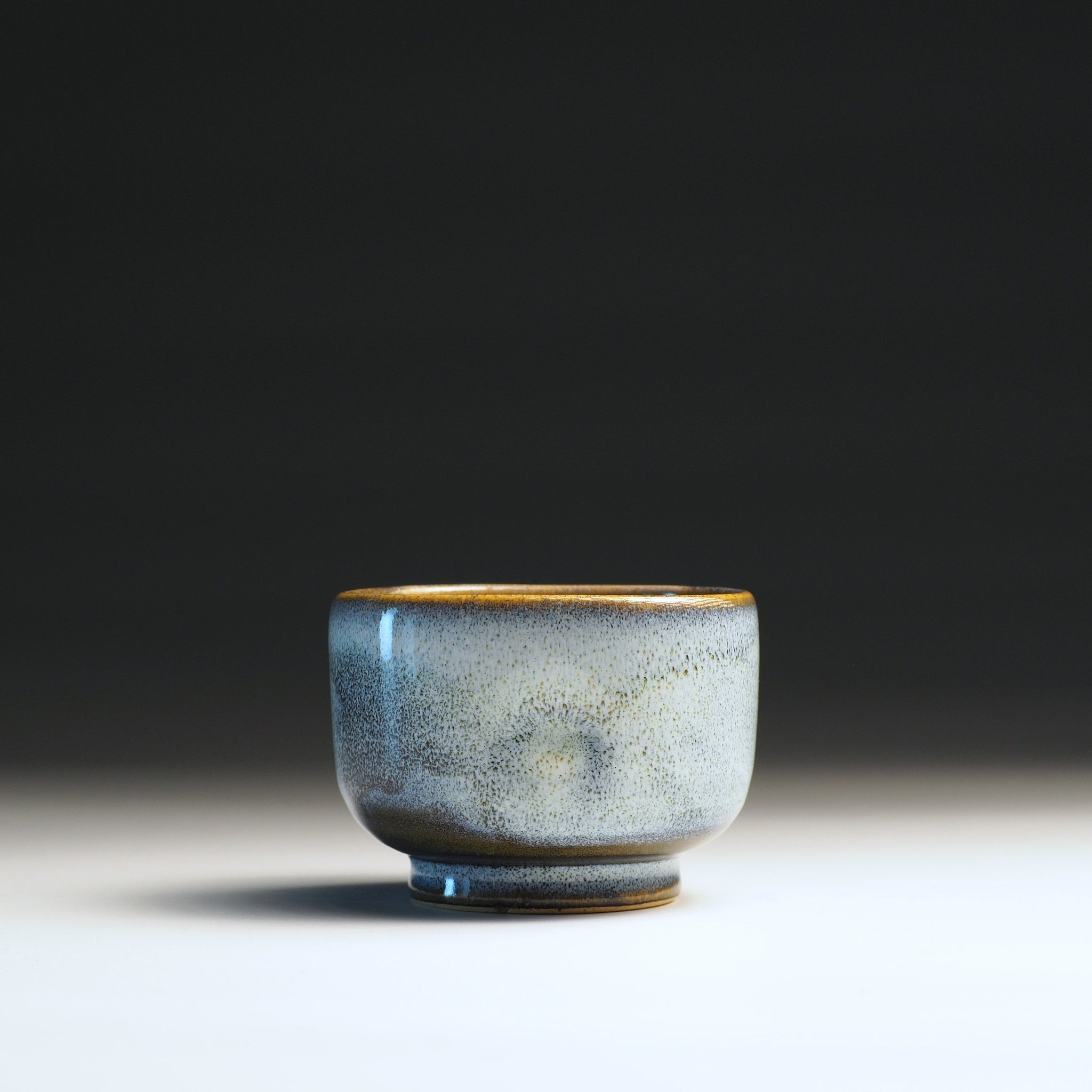 Japanese ceramic teacup with wabi sabi glaze and golden rim on a gradient background