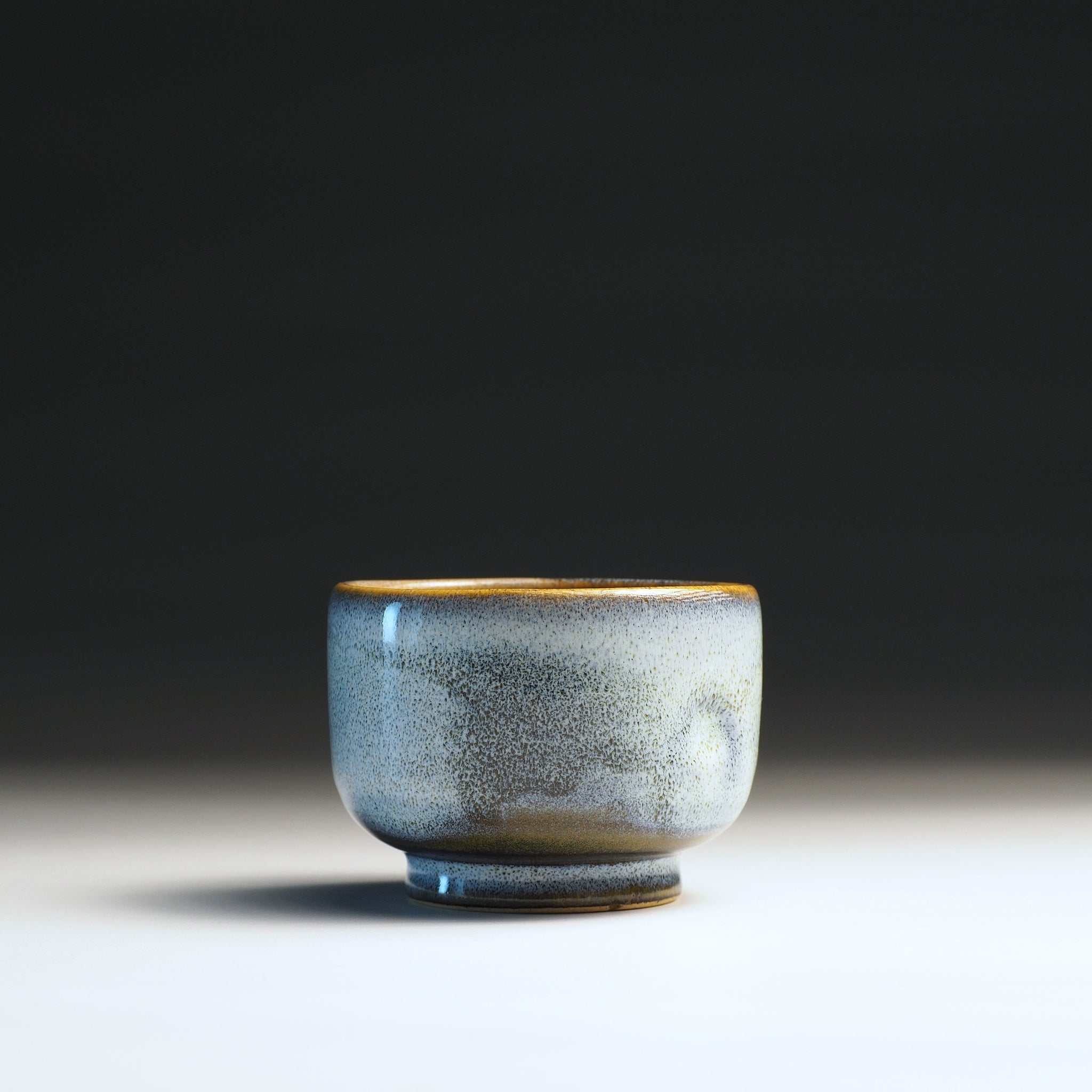 Frontal view of an azure Japanese ceramic teacup with wabi-sabi glaze and golden rim.