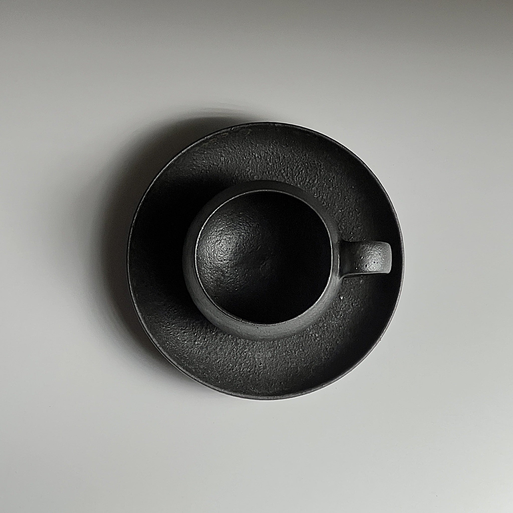 Top view of handcrafted black Japanese ceramic espresso cup and saucer on a beige background, Tsukushi