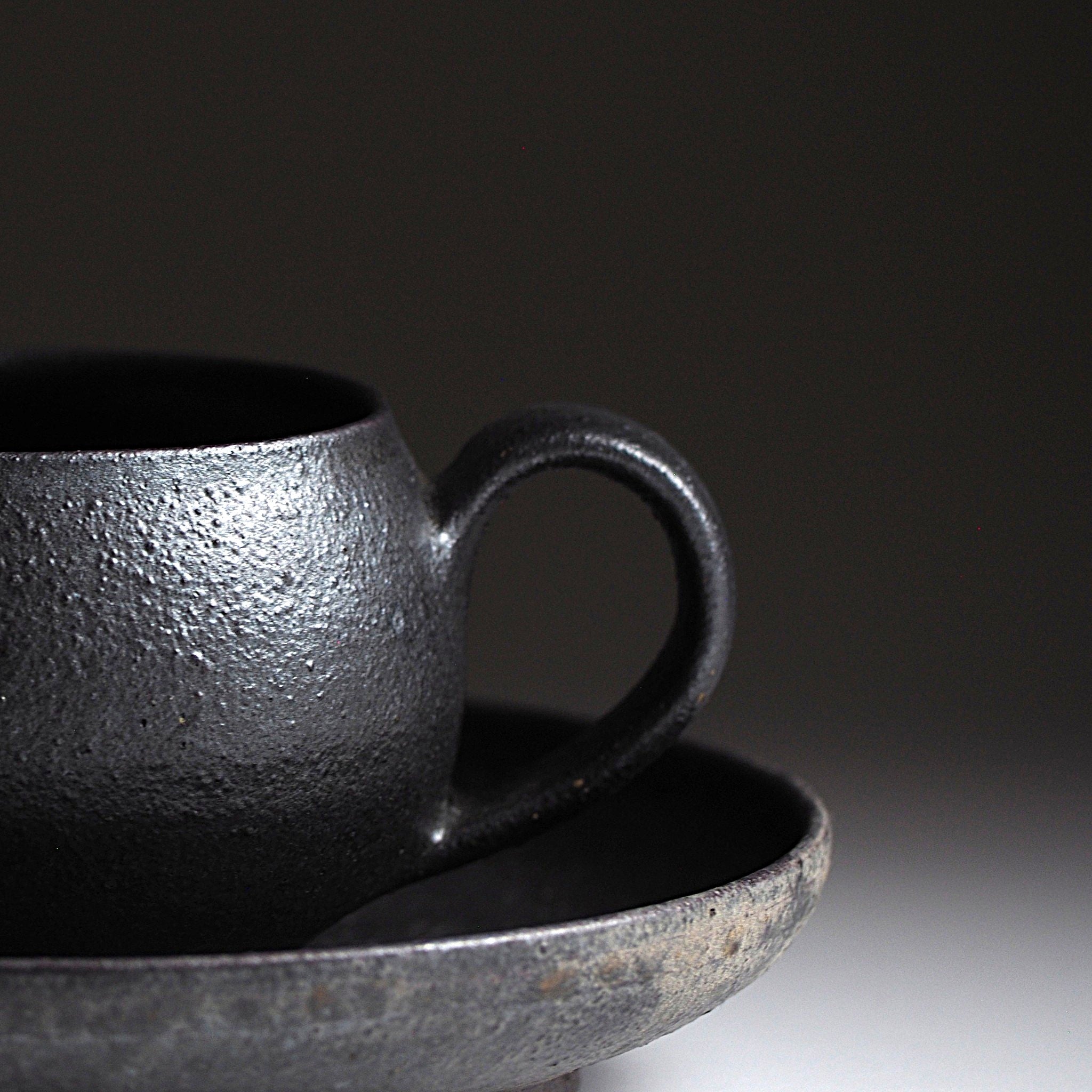 Close-up of handcrafted black Japanese ceramic espresso cup and saucer set on a dark background, Tsukushi