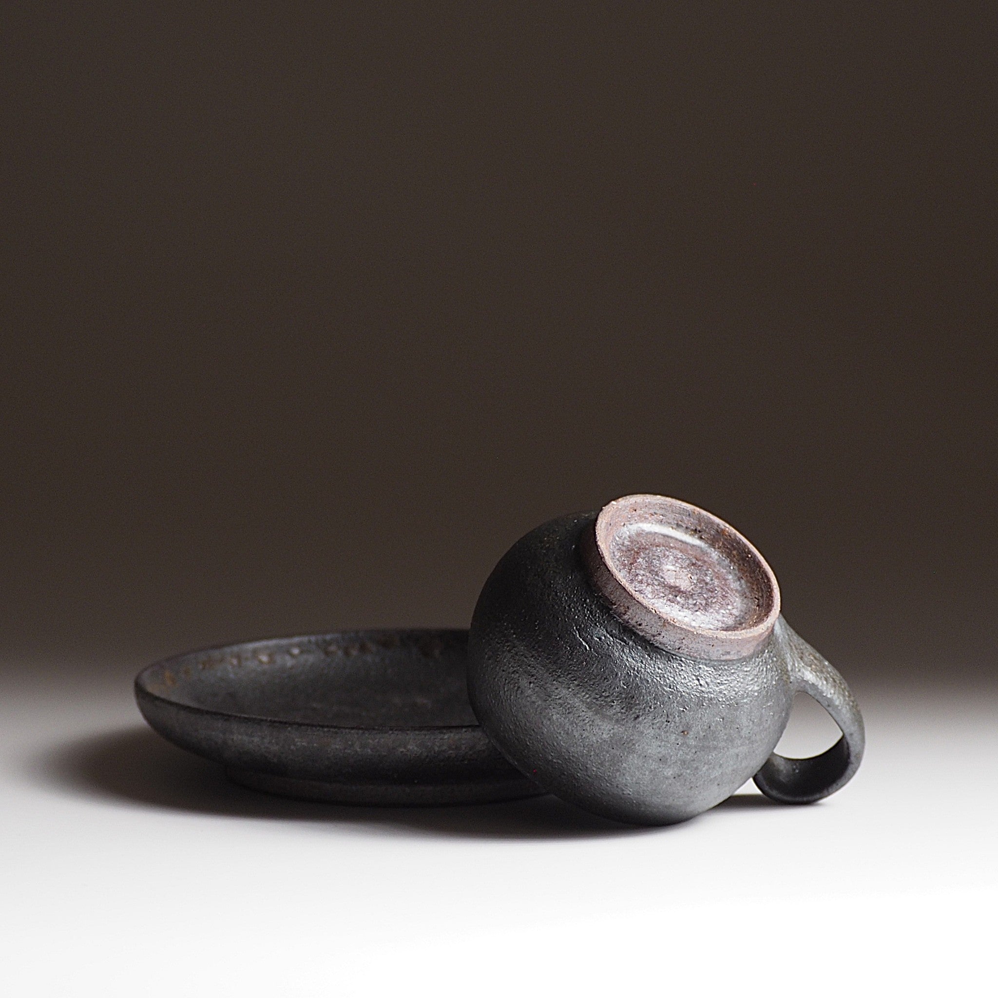 Bottom view of handcrafted black Japanese ceramic espresso cup and saucer on a dark background, Tsukushi