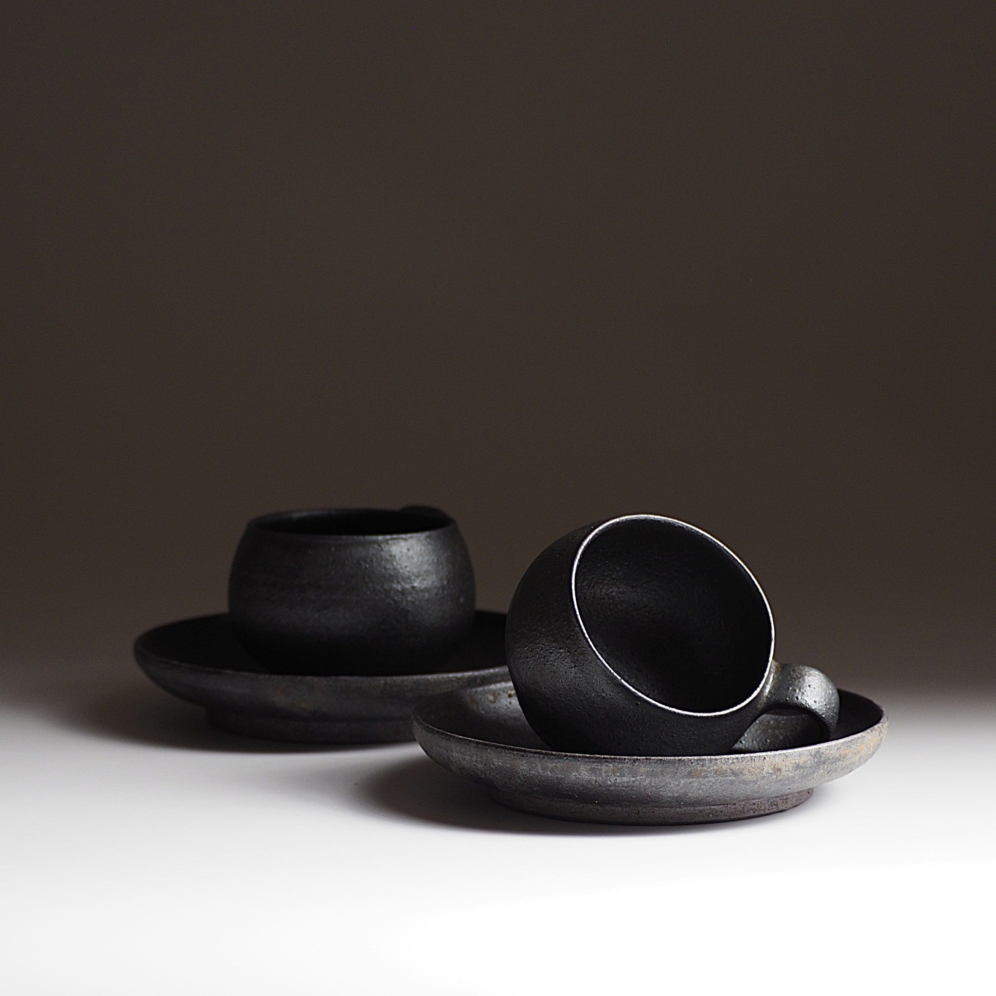 Two set of handcrafted black Japanese potteries espresso cup and saucer on a gray background, Tsukushi