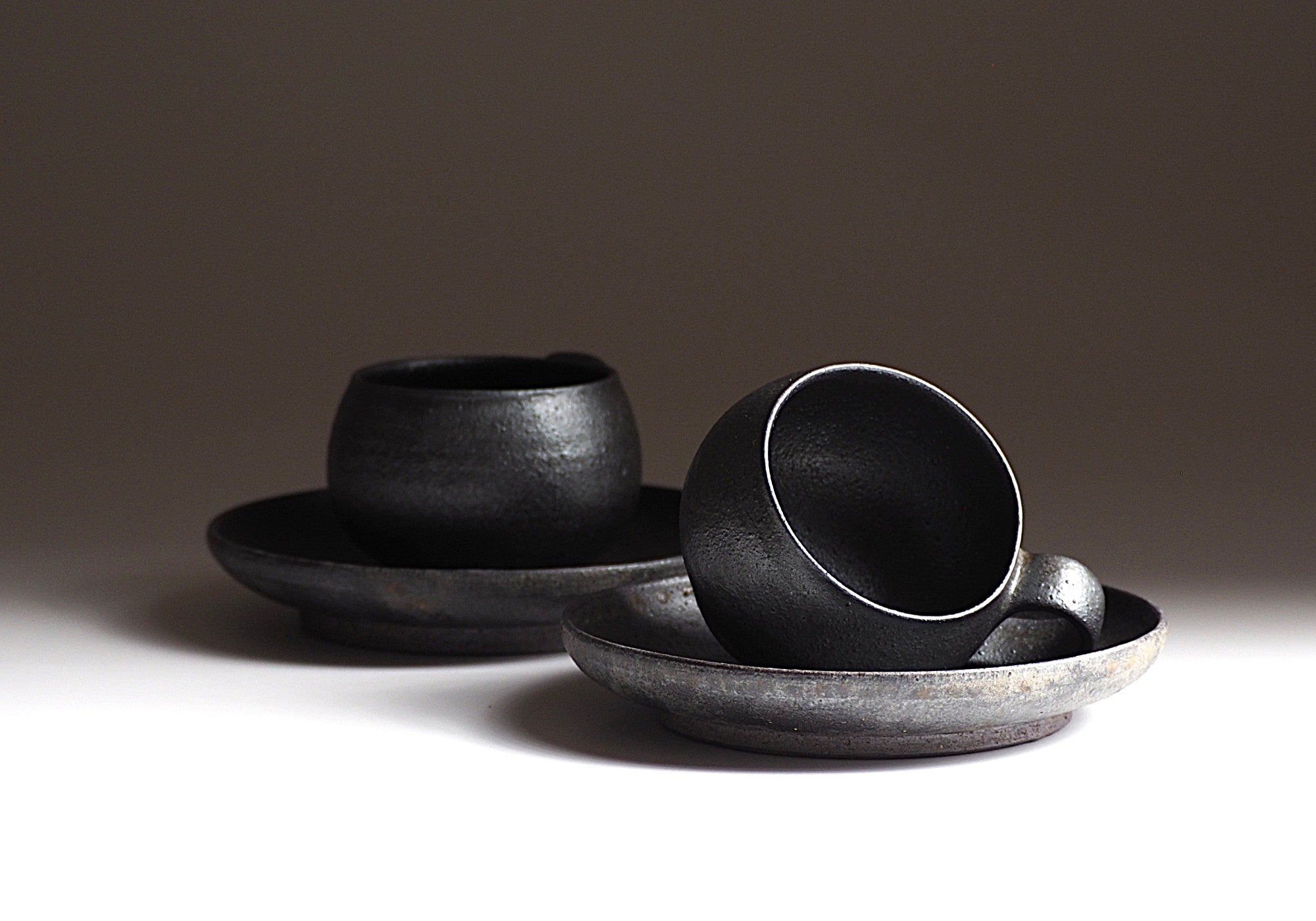 Two set of handcrafted black Japanese ceramic espresso cup and saucer on a light gray background, Tsukushi