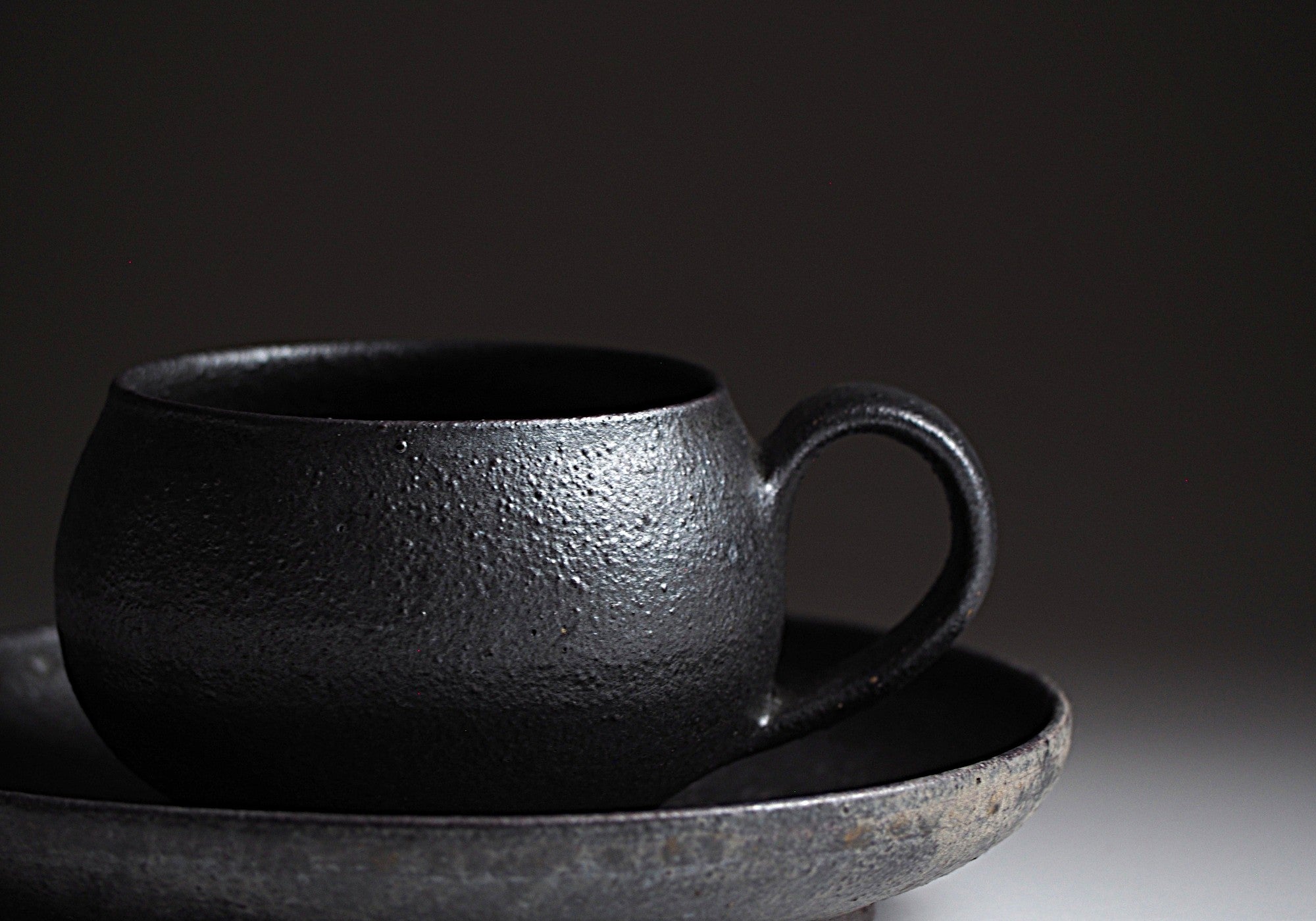 Close-up of handcrafted black Japanese ceramic espresso cup and saucer on a dark background, Tsukushi