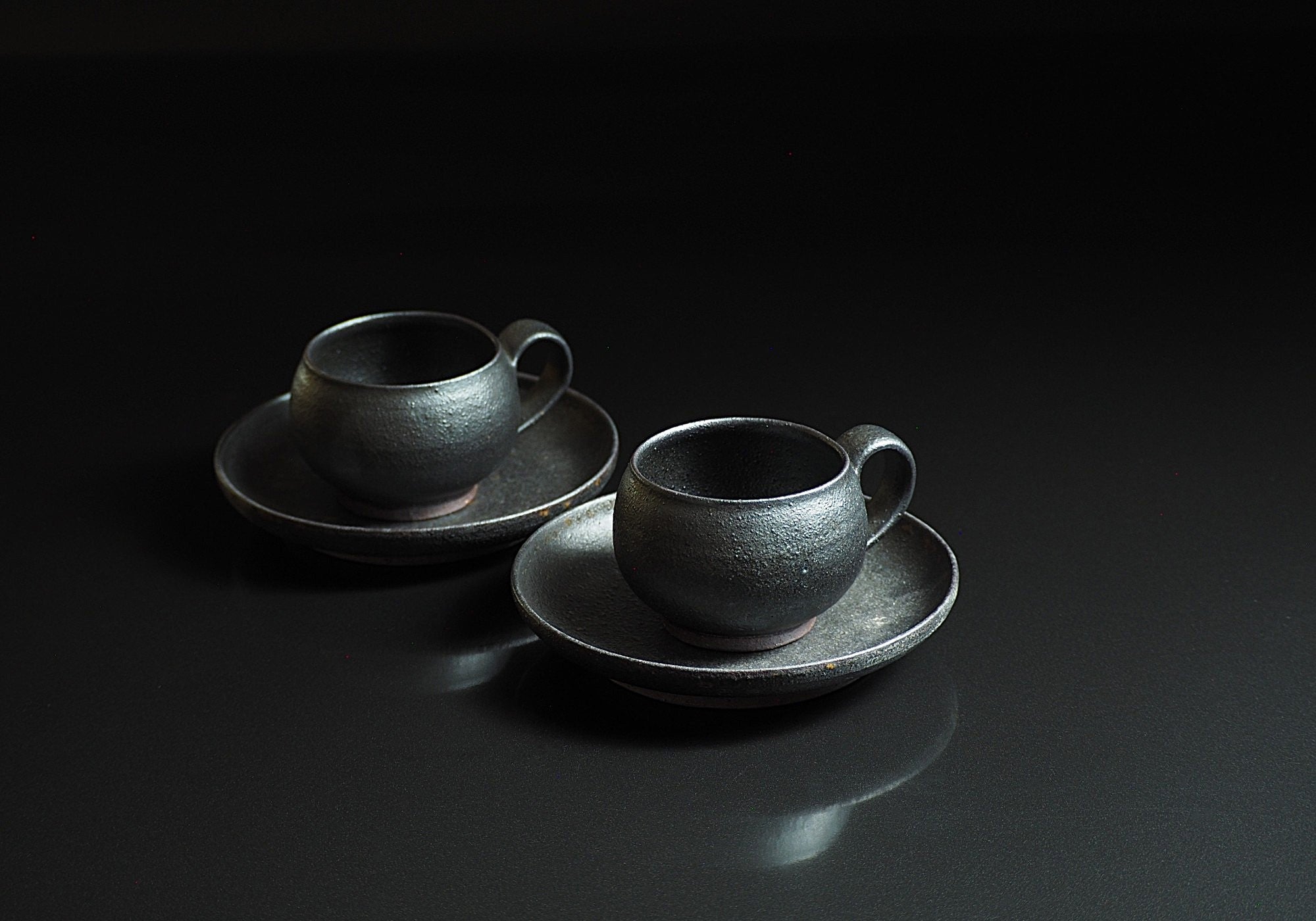 Two set of handcrafted black Japanese ceramic espresso cup and saucer on a black background, Tsukushi