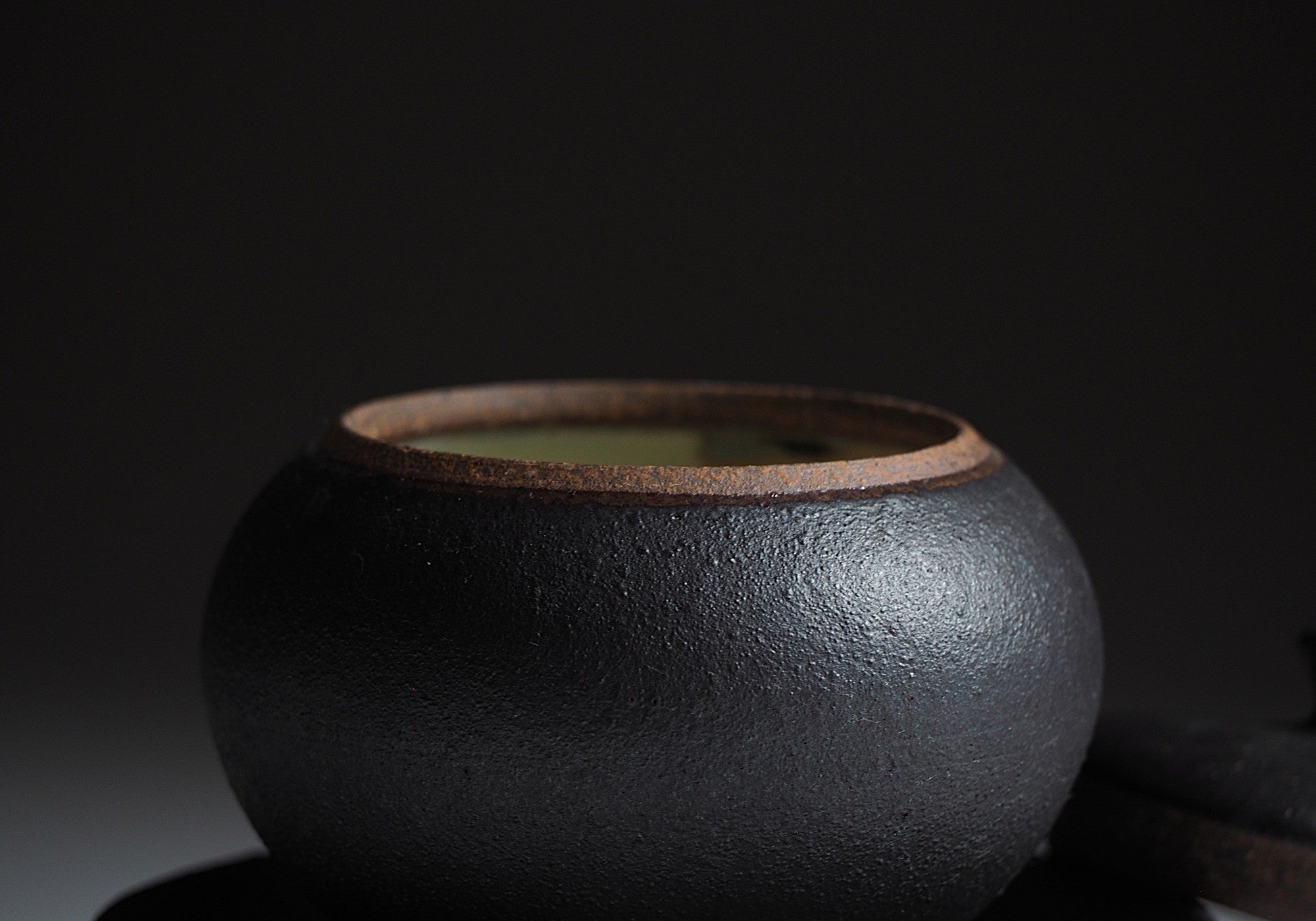 Detail of a black chawanmushi bowl in black on dark background. Tsukushi