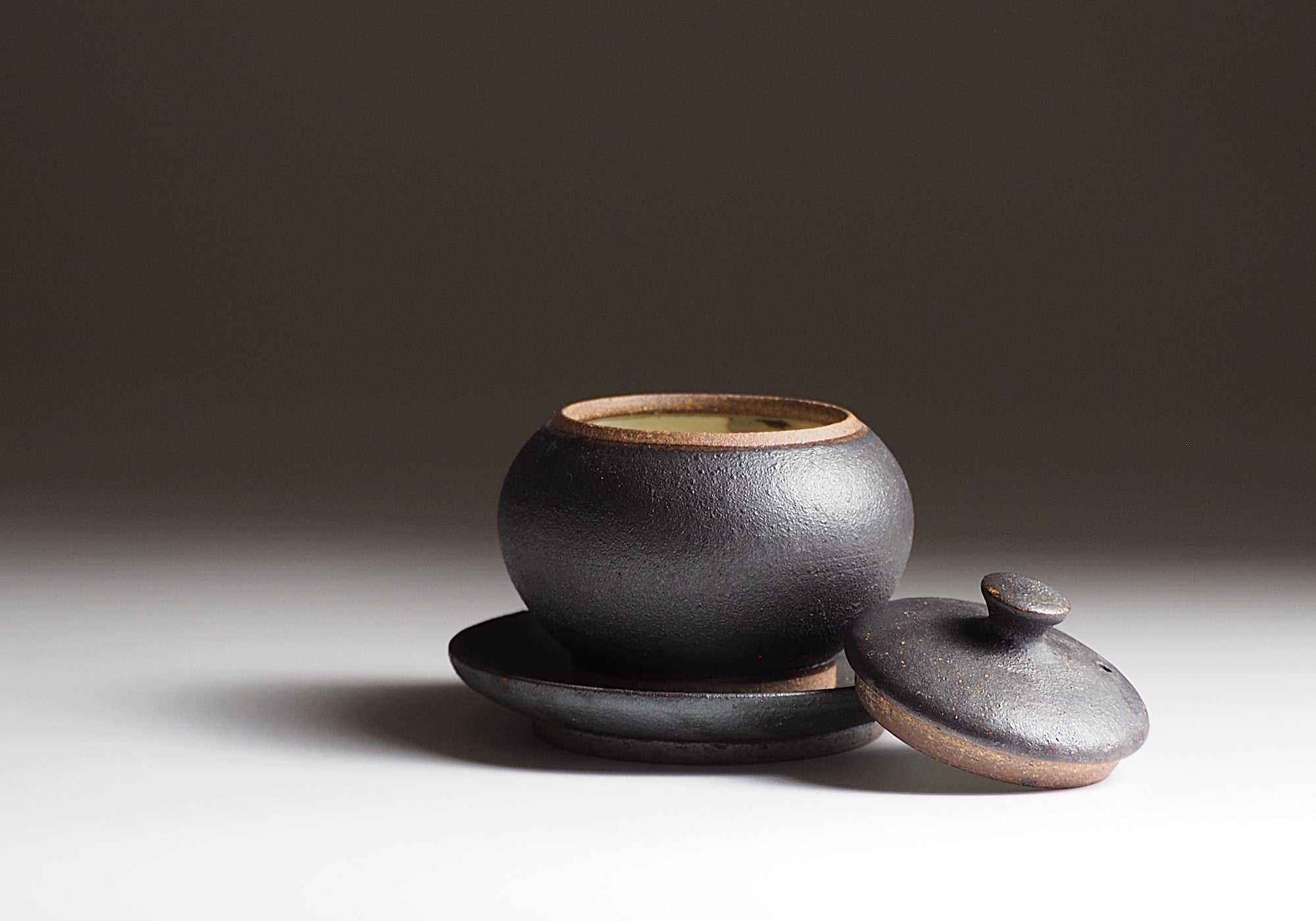 Black Japanese ceramic chawanmushi bowl with lid and saucer on faded background Tsukushi
