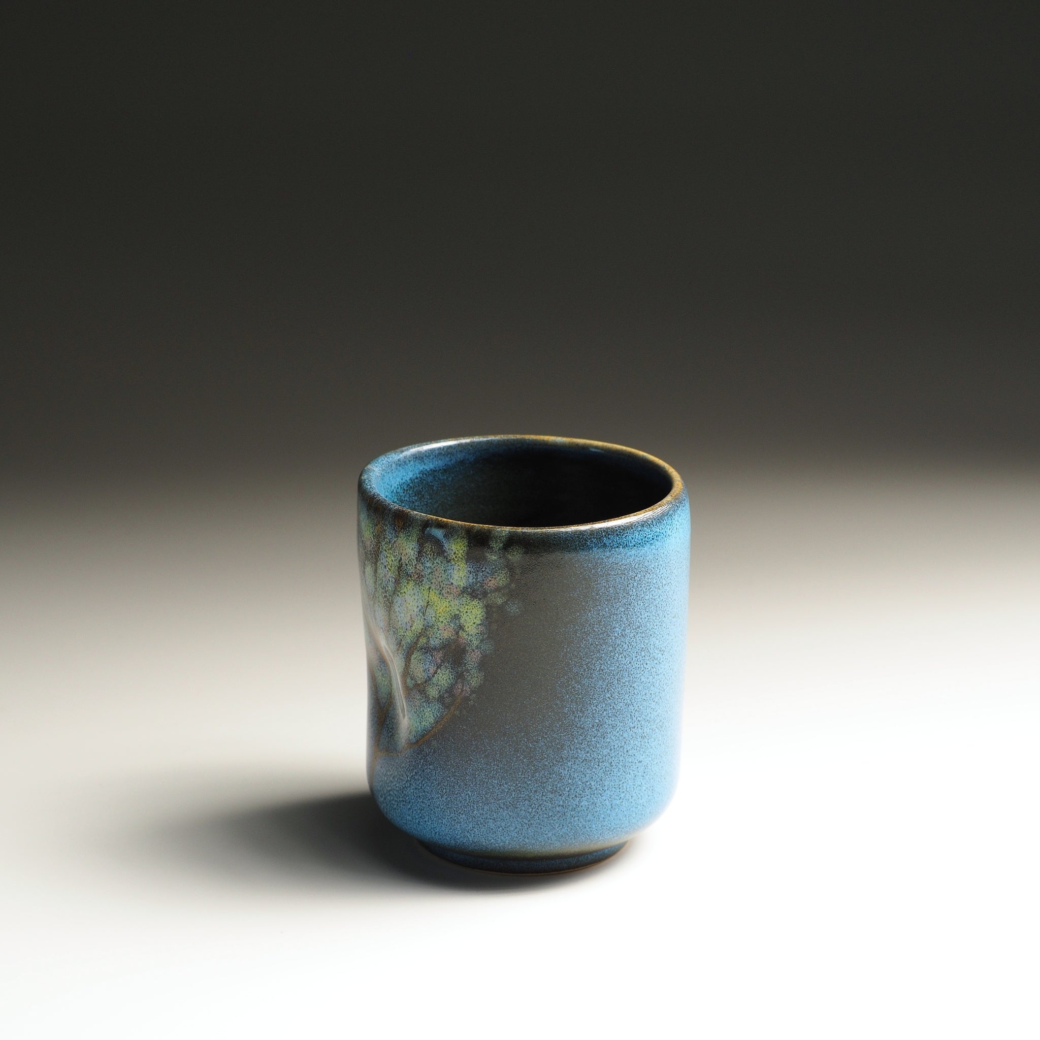 Side view of a ceramic yunomi cup with blue glaze and floral decotations. Tsukushi