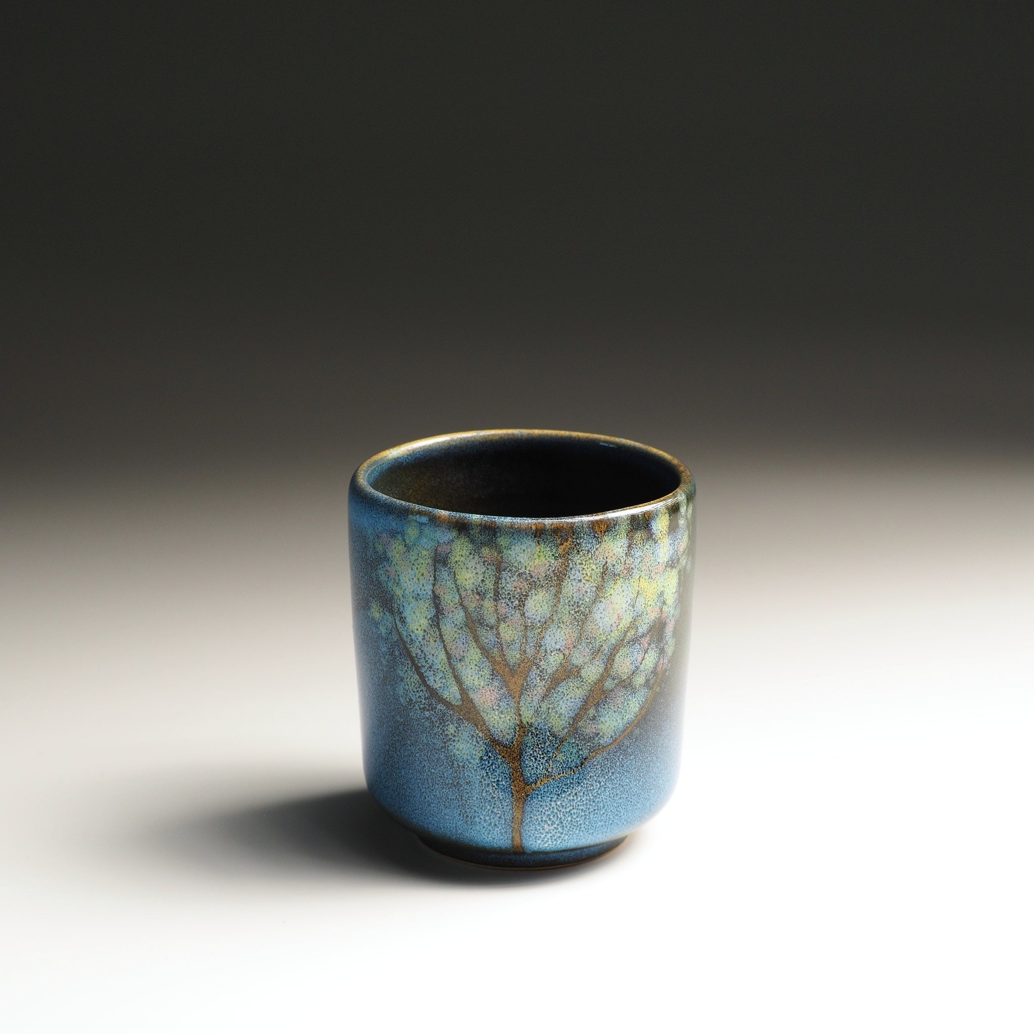 Japanese Yunomi Teacup with blue glaze and floreal motifs on a gradient background. Tsukushi