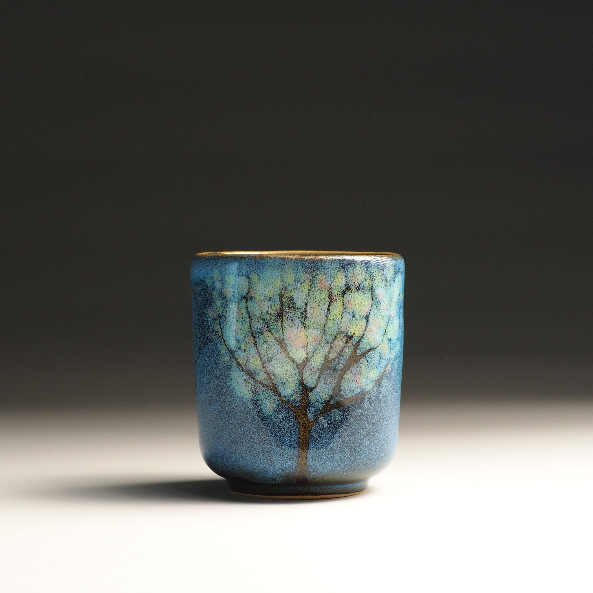 Full frontal view of a blue pottery yunomi teacup with tree design. Tsukushi