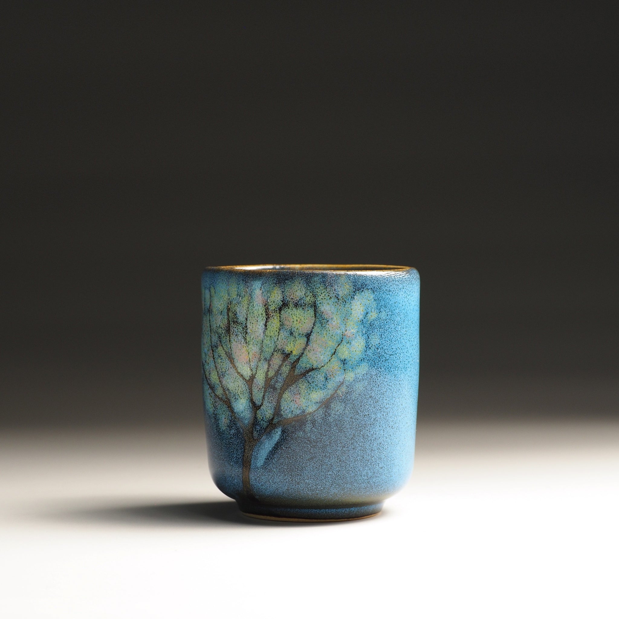 Front view of a handmade yunomi teacup with floral decorations and blue glaze. Tsukushi