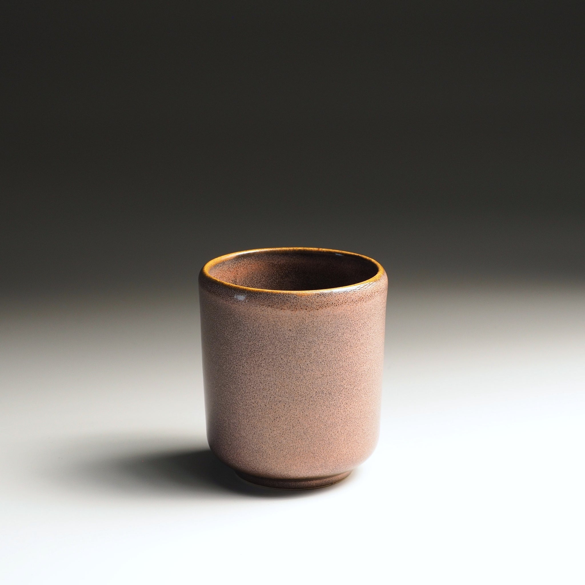 Back view of a handmade Japanese ceramic yunomi teacup in soft pink-brown wabi-sabi glaze with a warm golden rim ring, Tsukushi