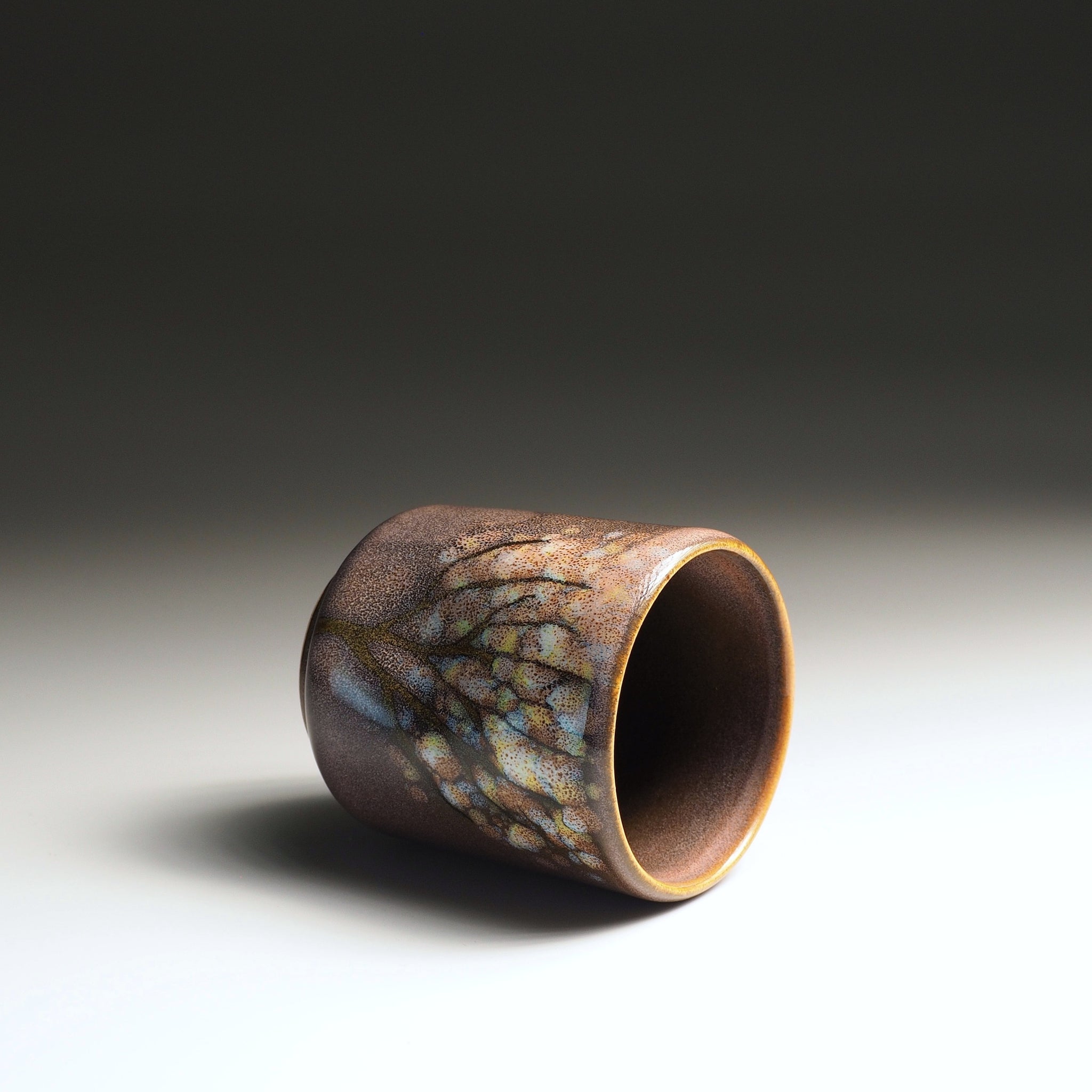 Side view of a handmade Japanese ceramic yunomi teacup with pink-brown wabi-sabi glaze and subtle iridescent patterning, Tsukushi