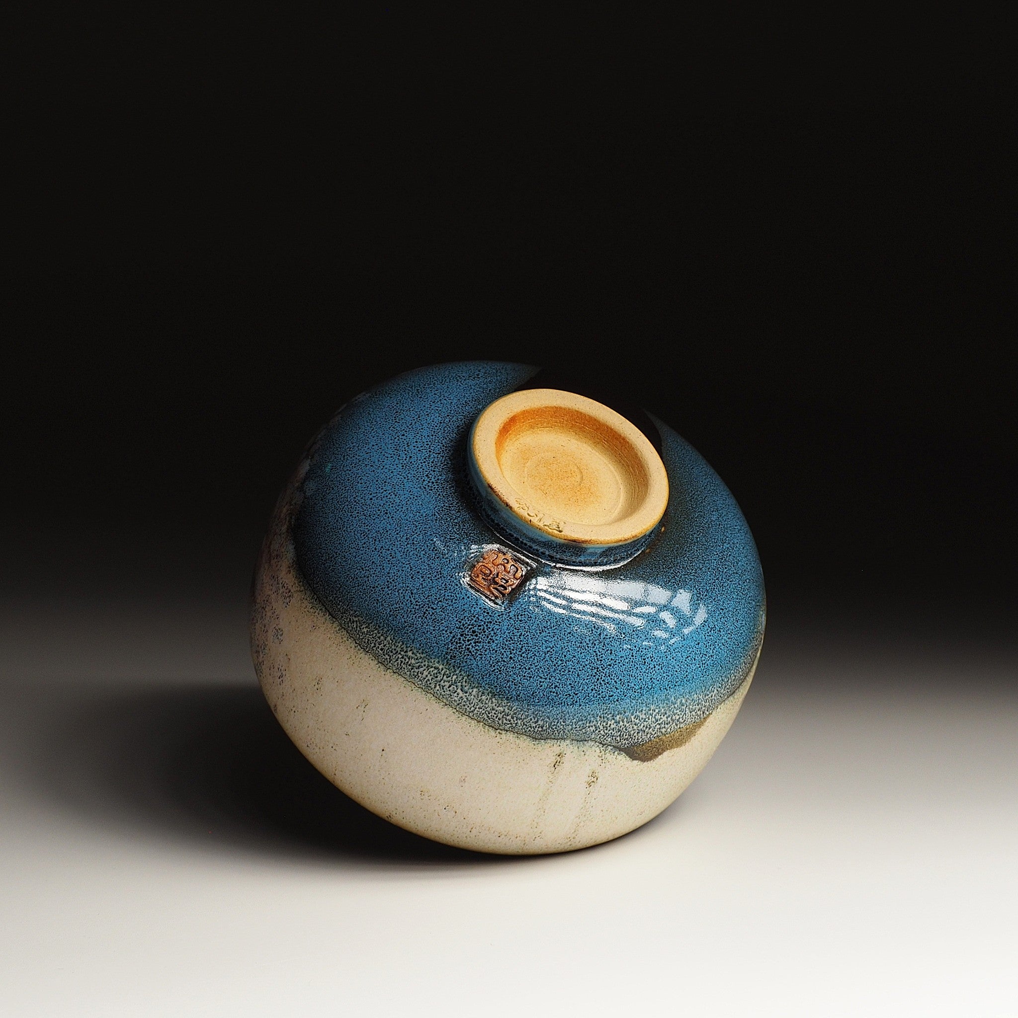 A bottom side of a Japanese ceramic matcha bowl designed with a tranquil lake against a black background. Tsukushi