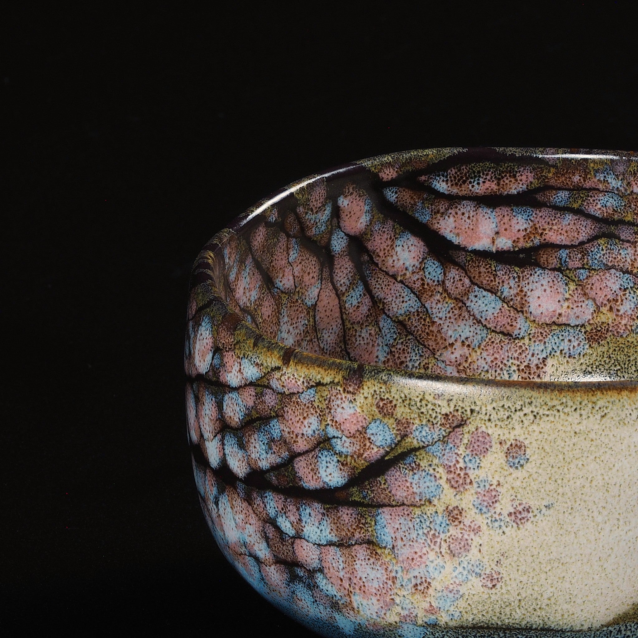 A close-up of a Japanese ceramic matcha bowl designed with cherry blossoms on a brown surface against a black background. Tsukushi.