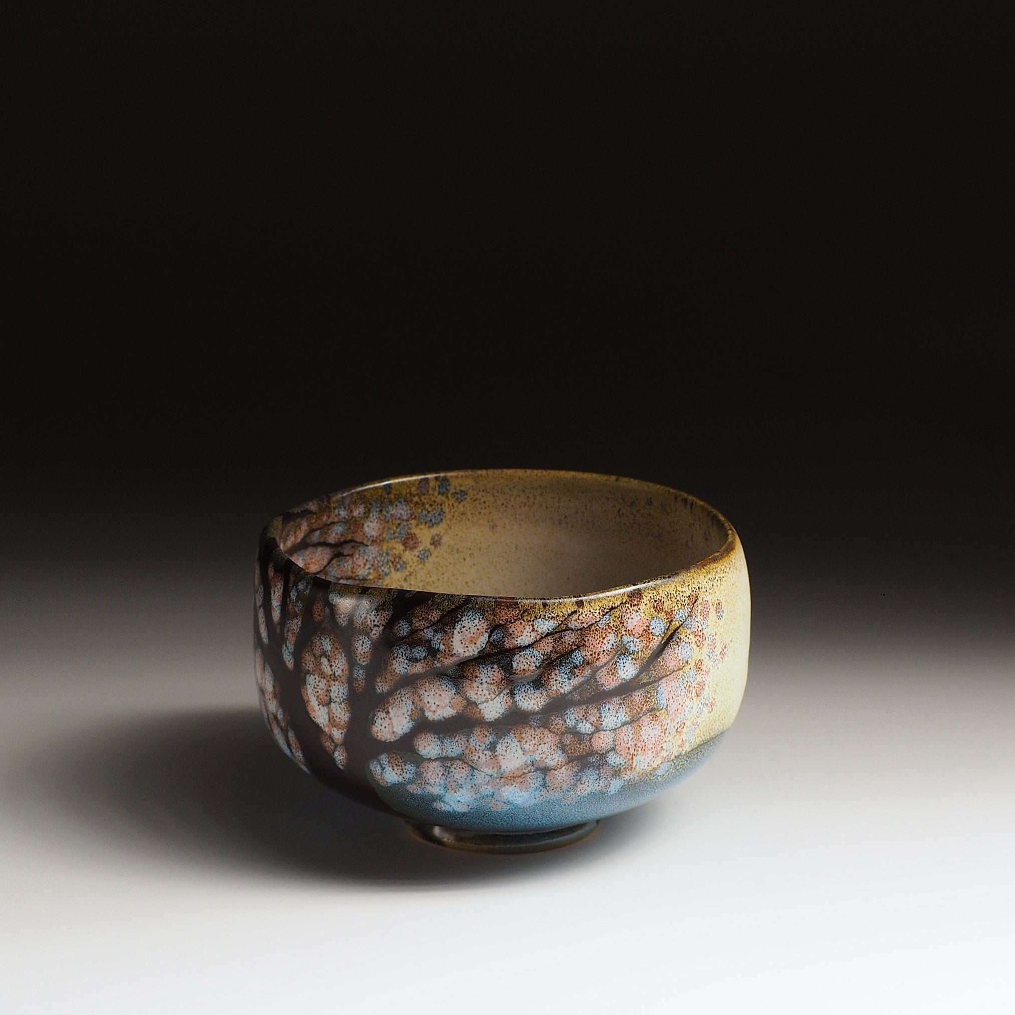 A Japanese Ceramic Maccha bowl with cherry blossoms and lake pattern on a dark background. Tsukushi