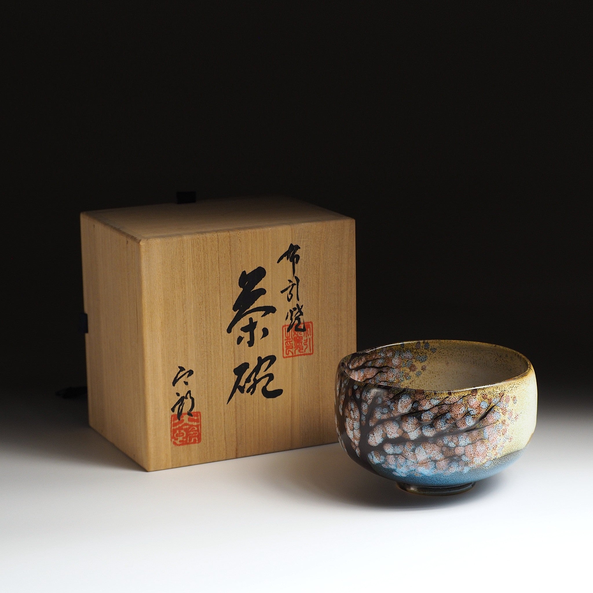 A Japanese Ceramic Maccha bowl with wooden box featuring calligraphy on a dark background. Tsukushi