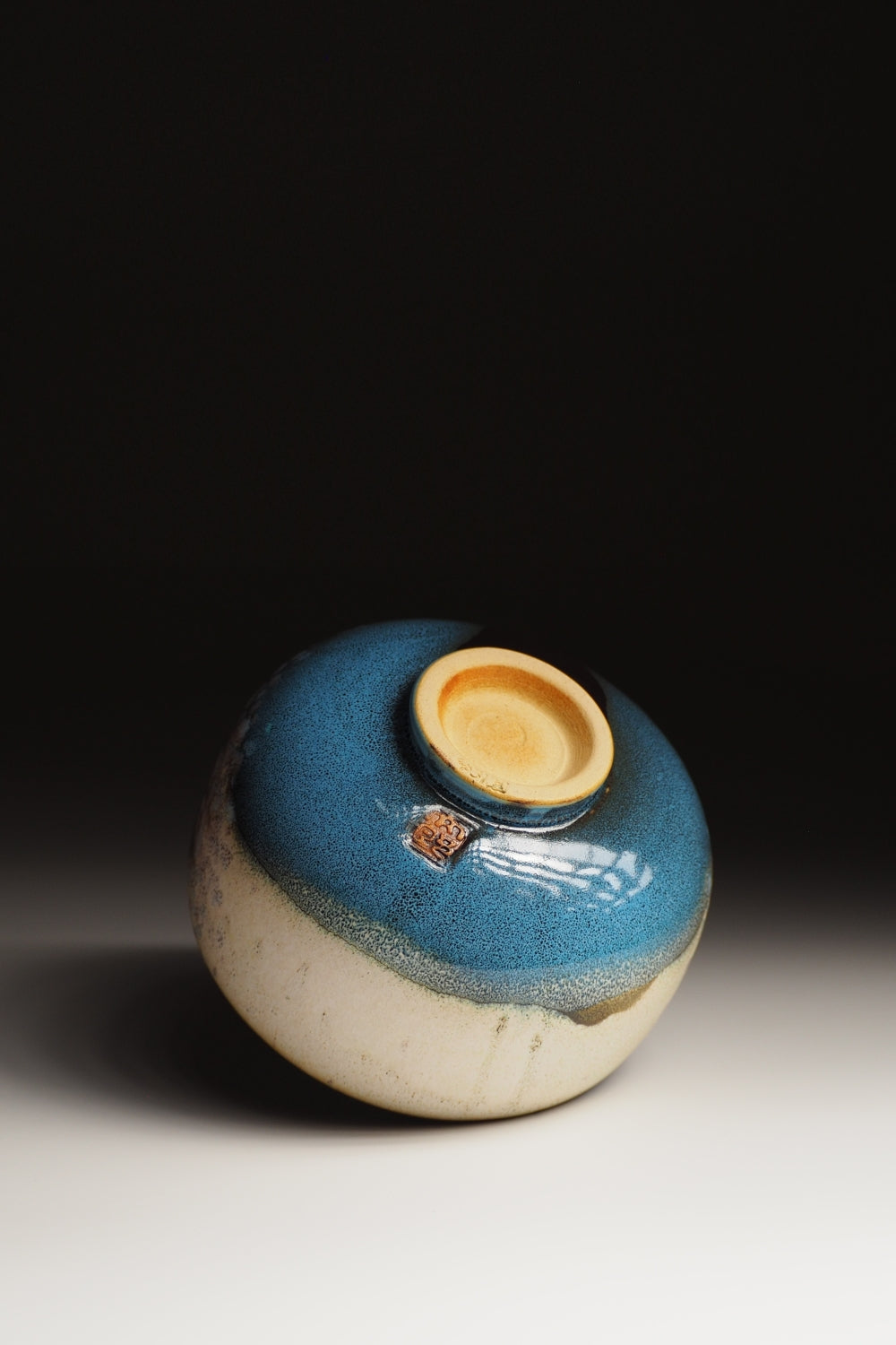 bottom view of a matcha bowl with blue glaze on a dark background. Tsukushi