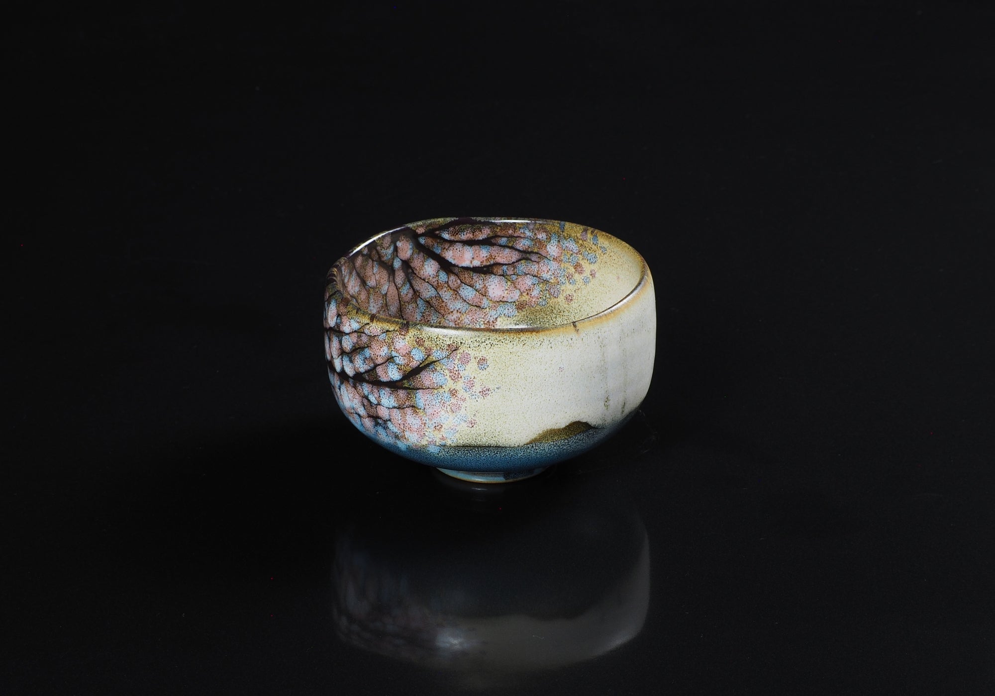 A Japanese ceramic matcha bowl designed with cherry blossoms against a black background. Tsukushi