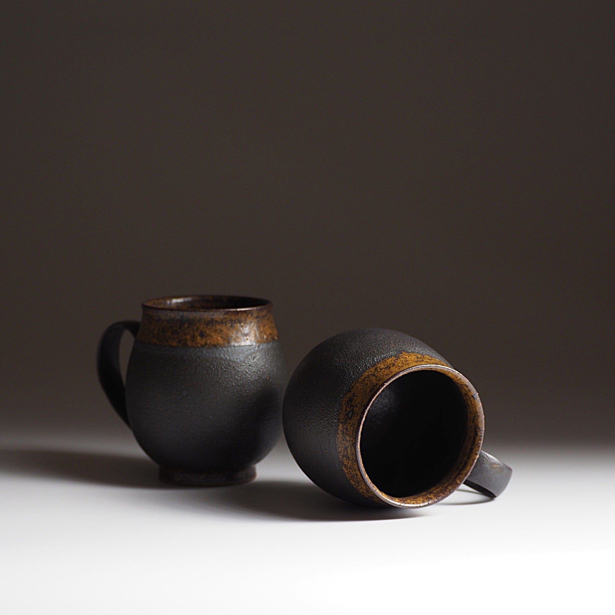 Handcrafted two black Japanese ceramic tea mugs with brown accents on a gradation background, Tsukushi