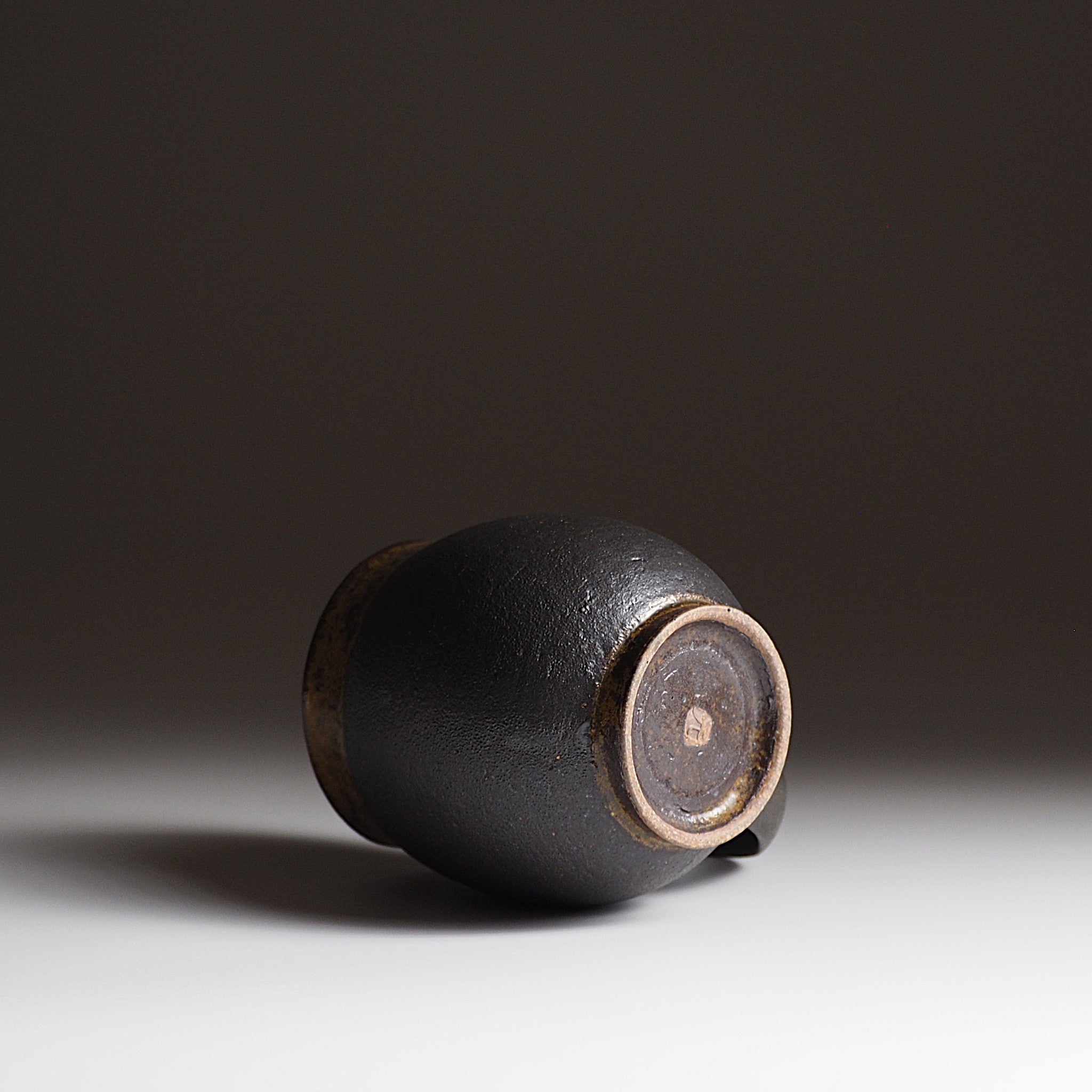Bottom view of handcrafted black Japanese ceramic tea mug on a white surface with a dark background, Tsukush