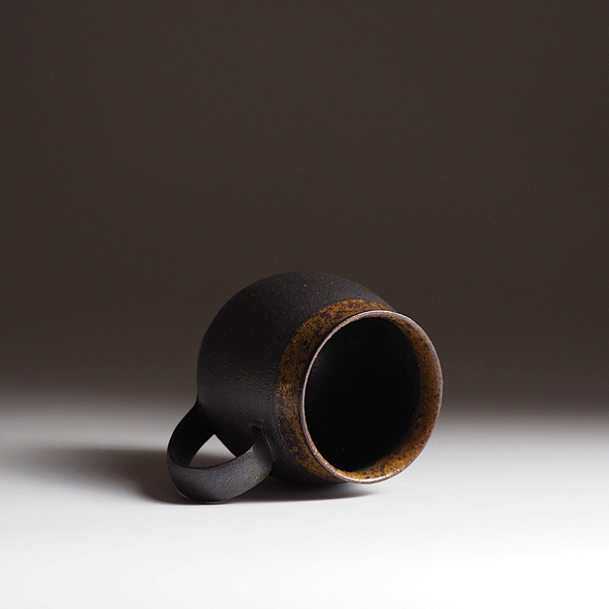 Handcrafted black Japanese ceramic tea mug on a white surface with a dark background, Tsukushi